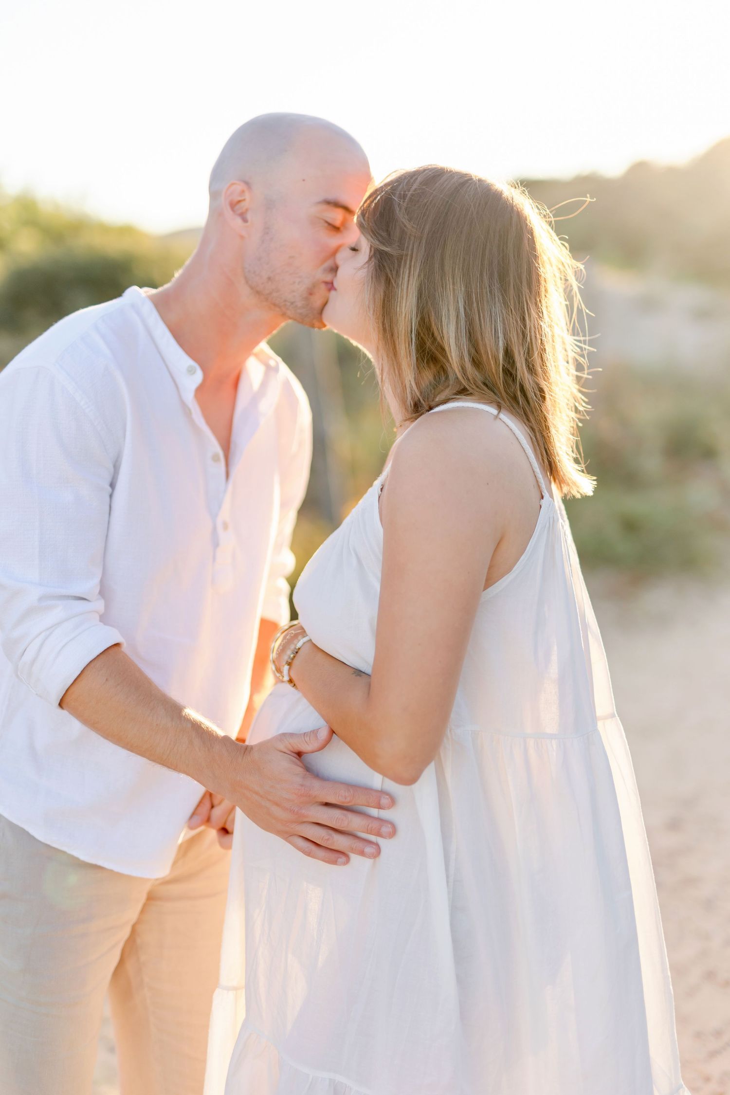 Romantic couple embraces during golden hour beach photoshoot wearing white outfits.