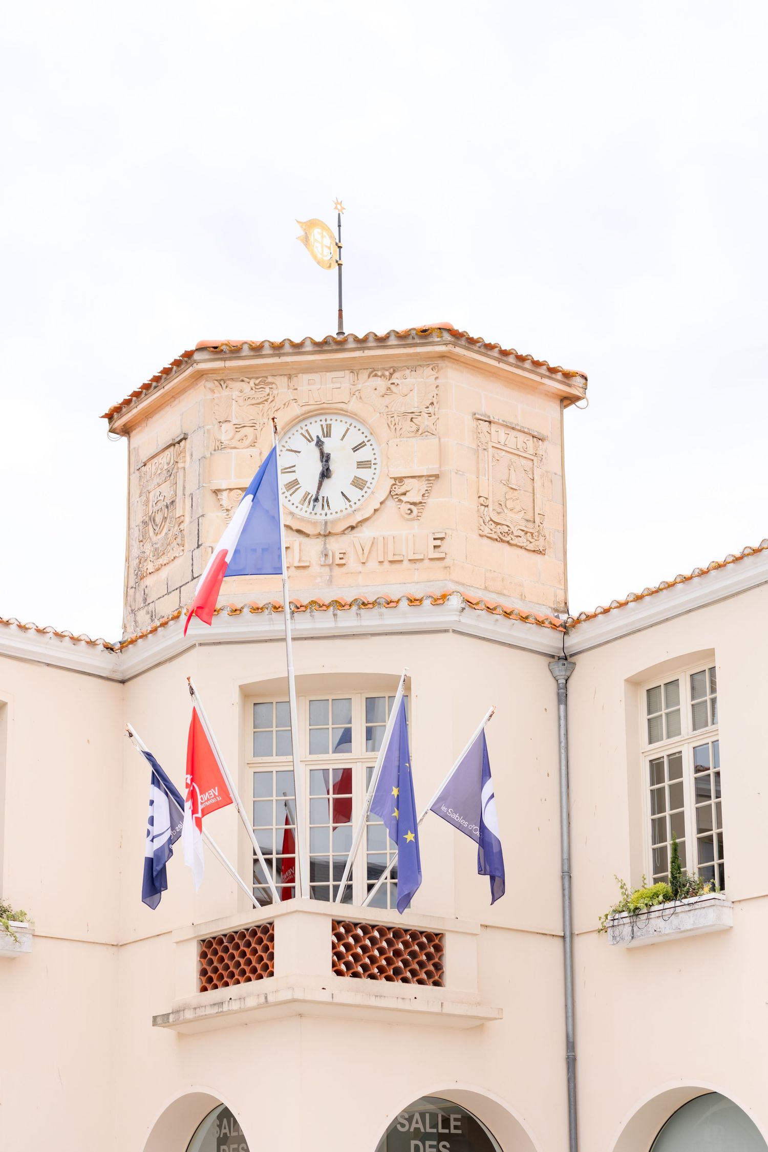 Beige Mediterranean style building with flags and white shuttered windows.