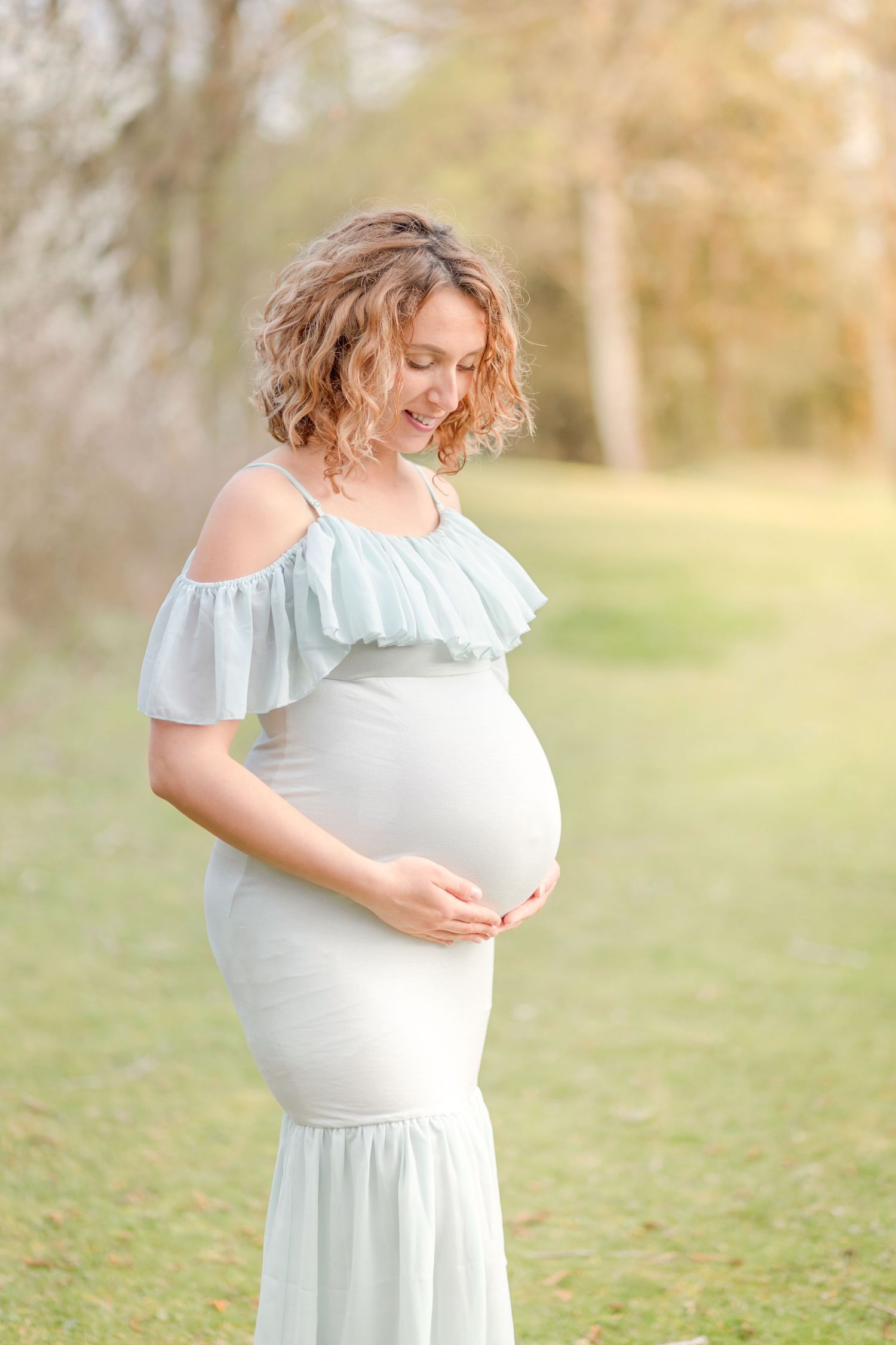 A maternity photo showcasing an elegant white off-shoulder dress in a sun-drenched outdoor setting.