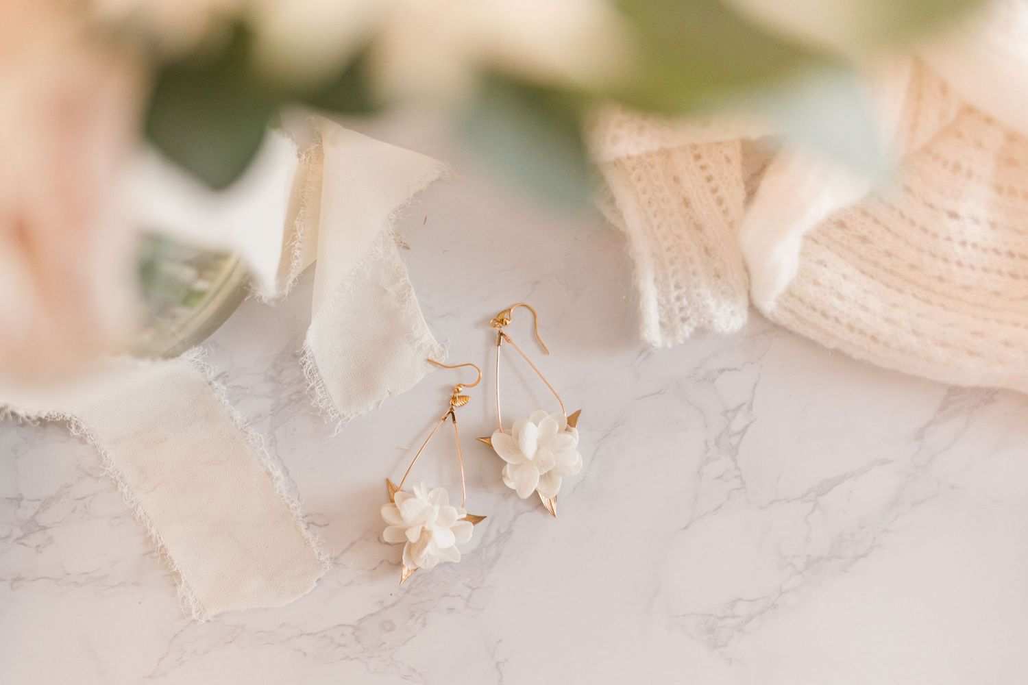 Delicate white earrings displayed on light marble surface with soft natural lighting.