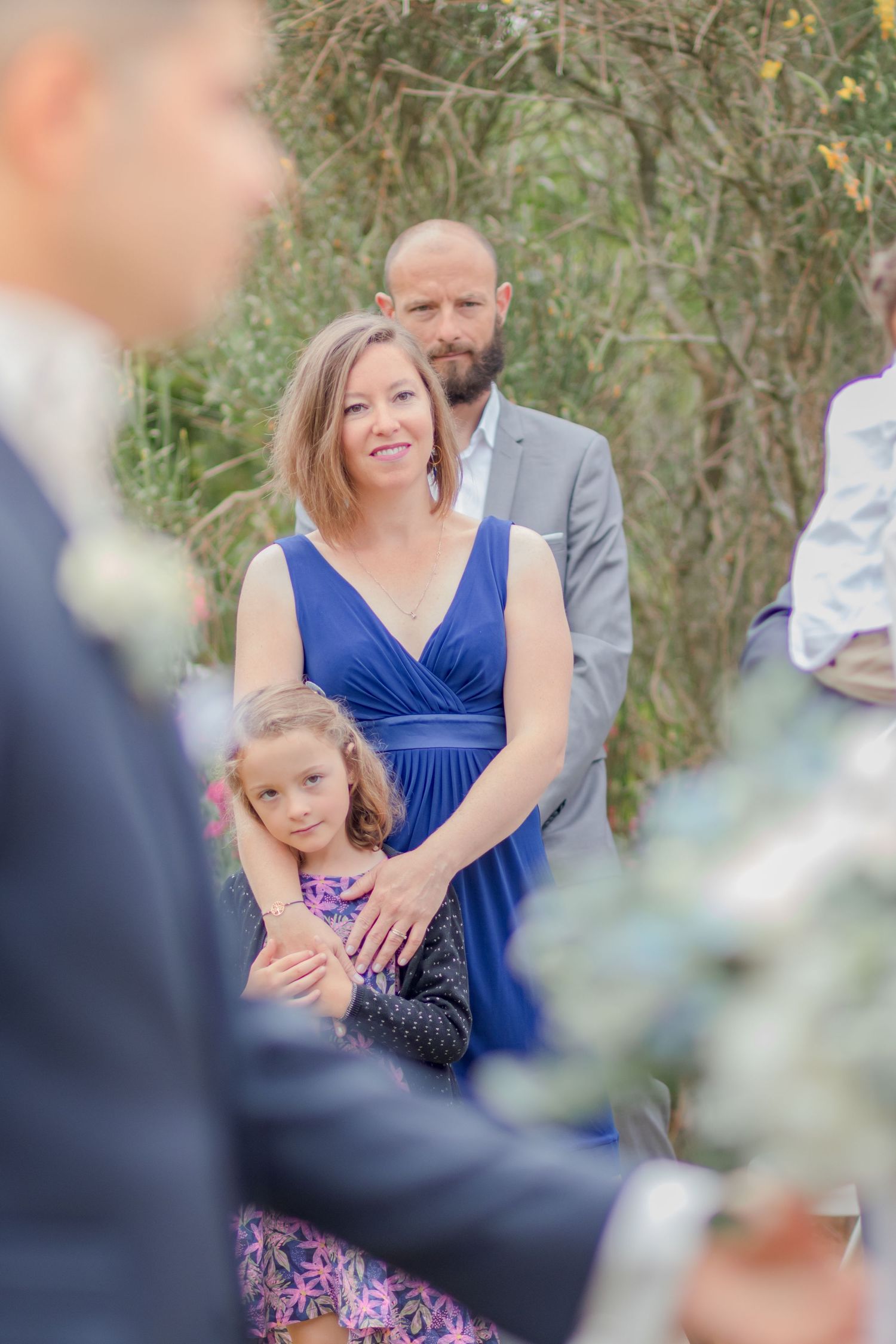 Wedding guests in blue dresses watching ceremony from garden seating area.