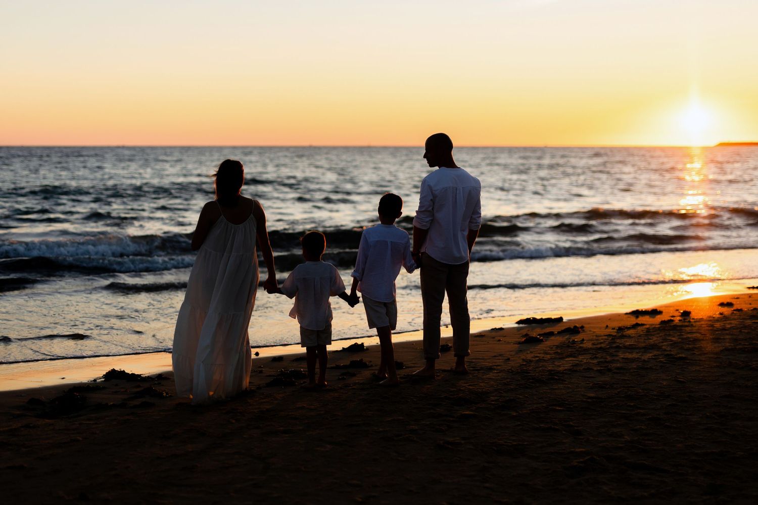 Family silhouette watching sunset together on beach with ocean waves.