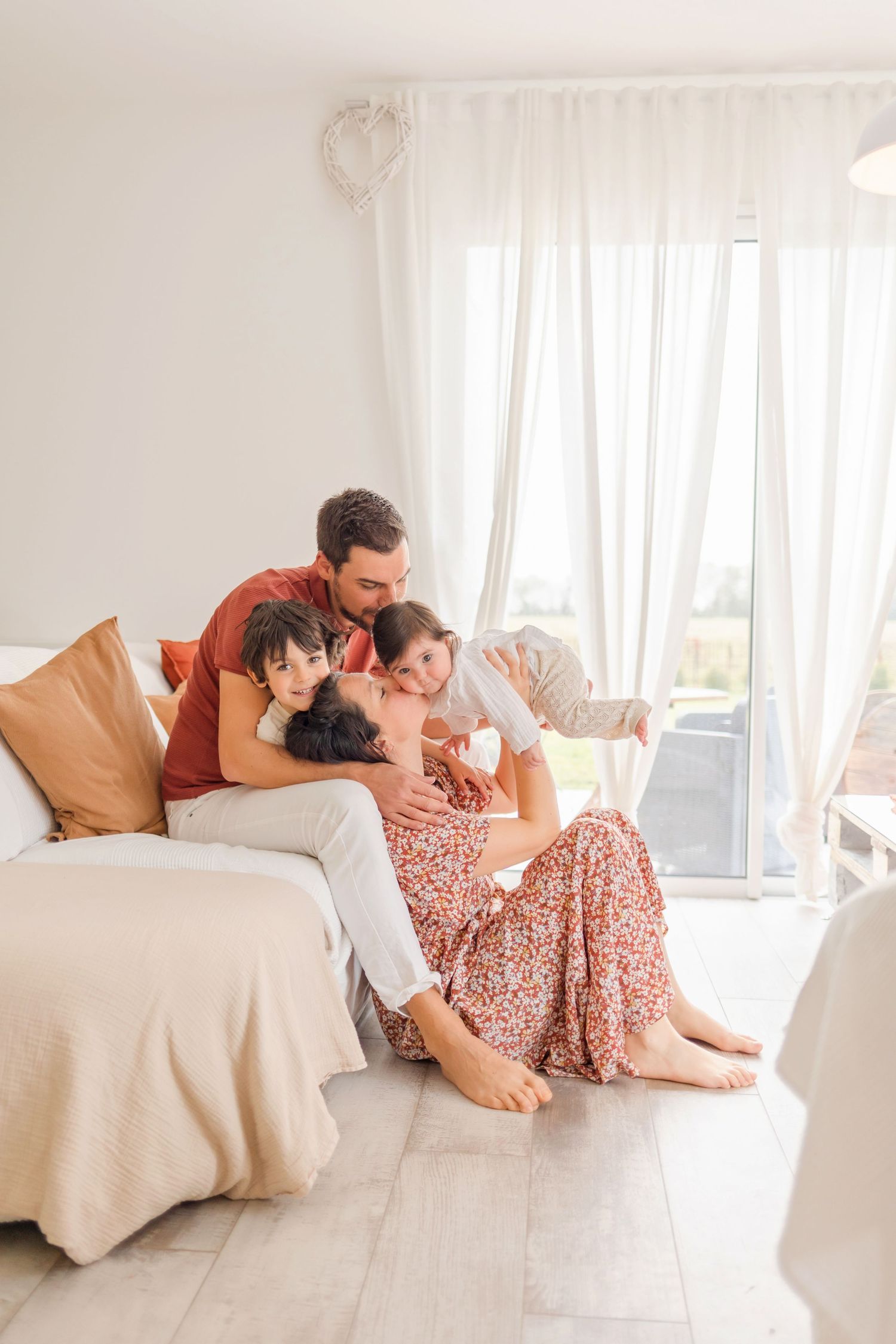 Family sharing affectionate moments together on a white couch with natural light streaming through windows.