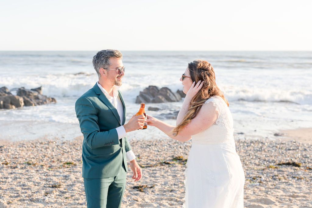 Newlyweds share drinks on a beach during sunset celebration.