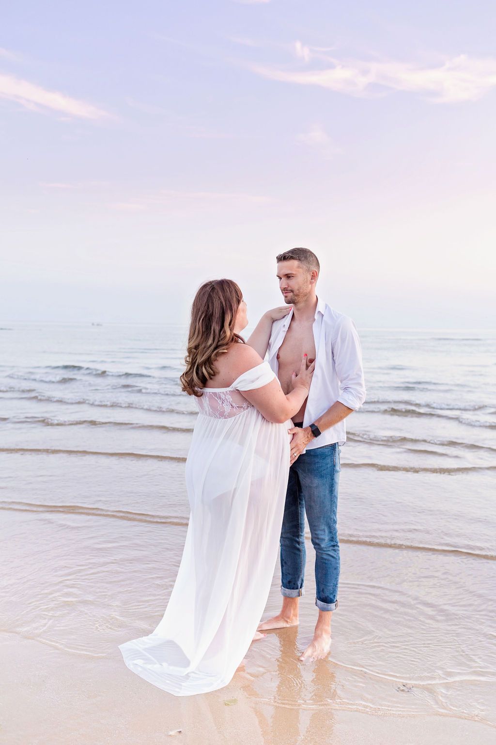 A couple laughs together during their beach maternity photo session at sunset.