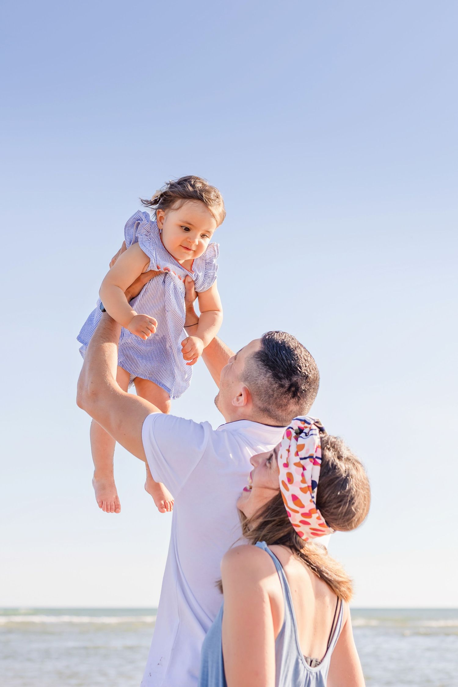 Playful family moment captured against bright blue sky at the beach.