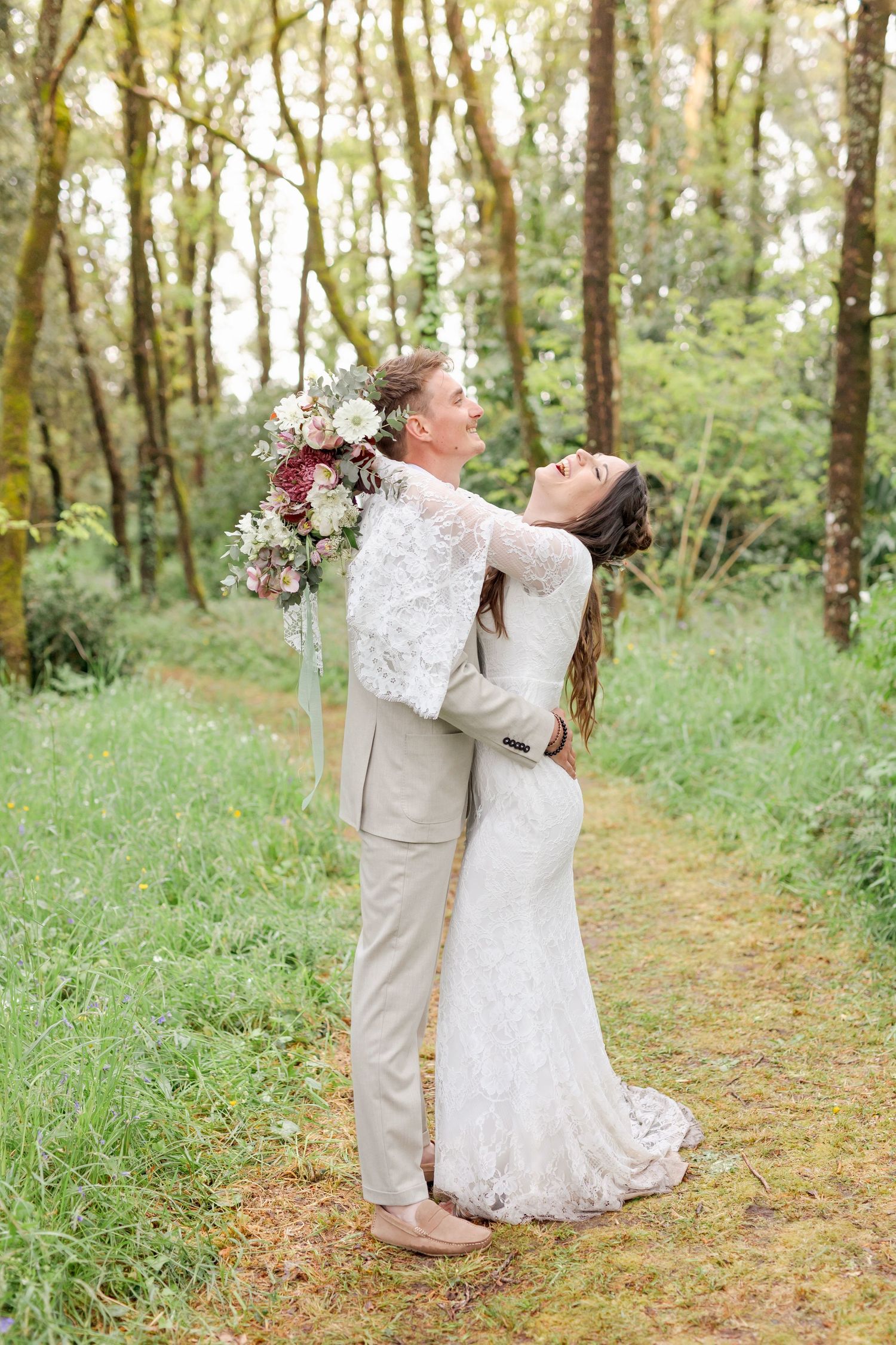 Wedding couple shares playful moments on a forest path surrounded by green foliage.