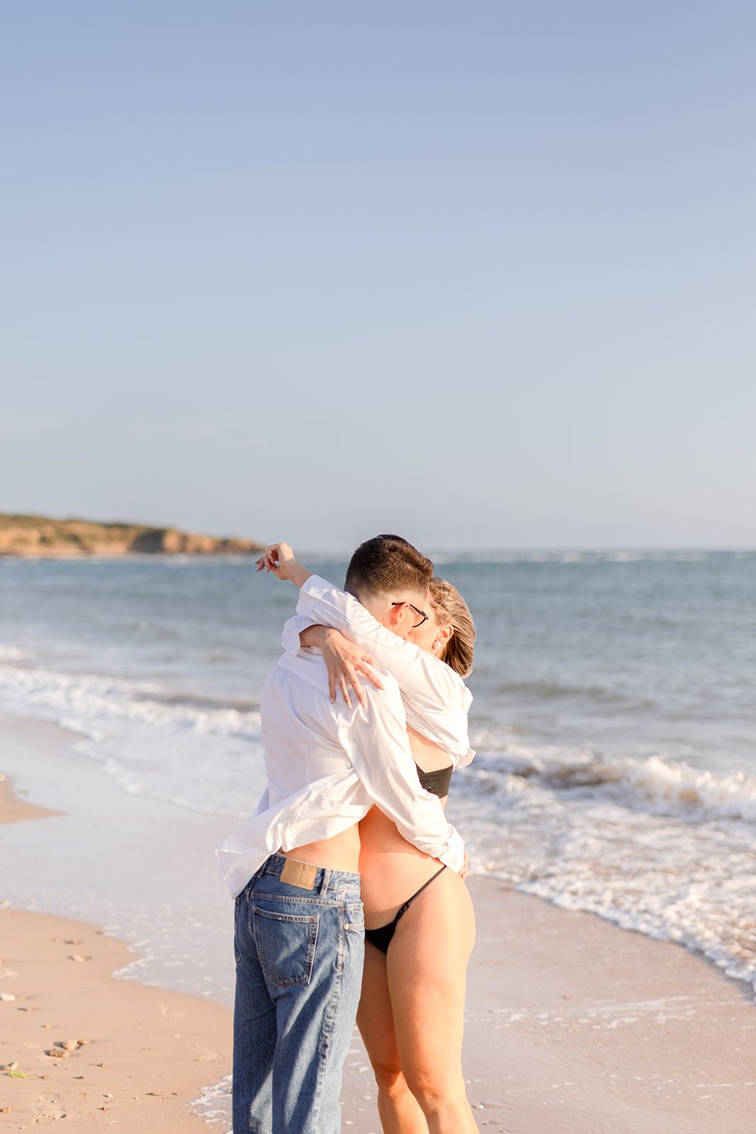 Two figures enjoying a carefree moment on a sandy beach with ocean waves in the background.