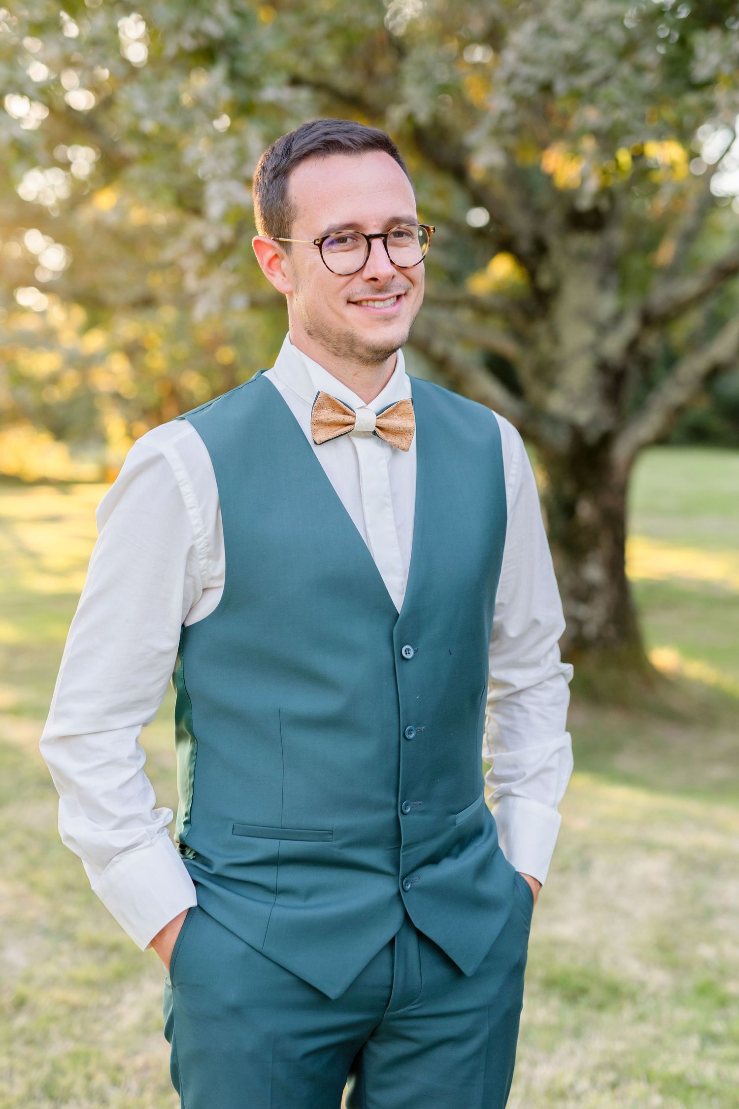 Portrait of a groom in a teal vest and bowtie smiling in an outdoor garden setting.