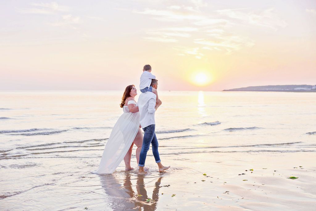 Couple walking along beach shore during golden sunset with soft waves.