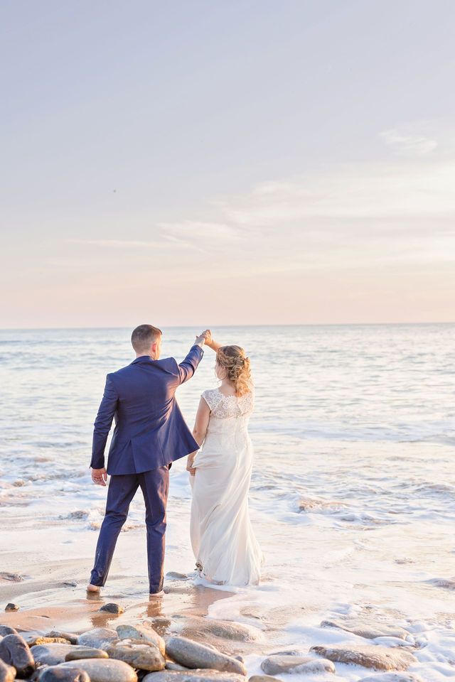 A romantic couple dances on a rocky beach at sunset while waves crash around their feet.