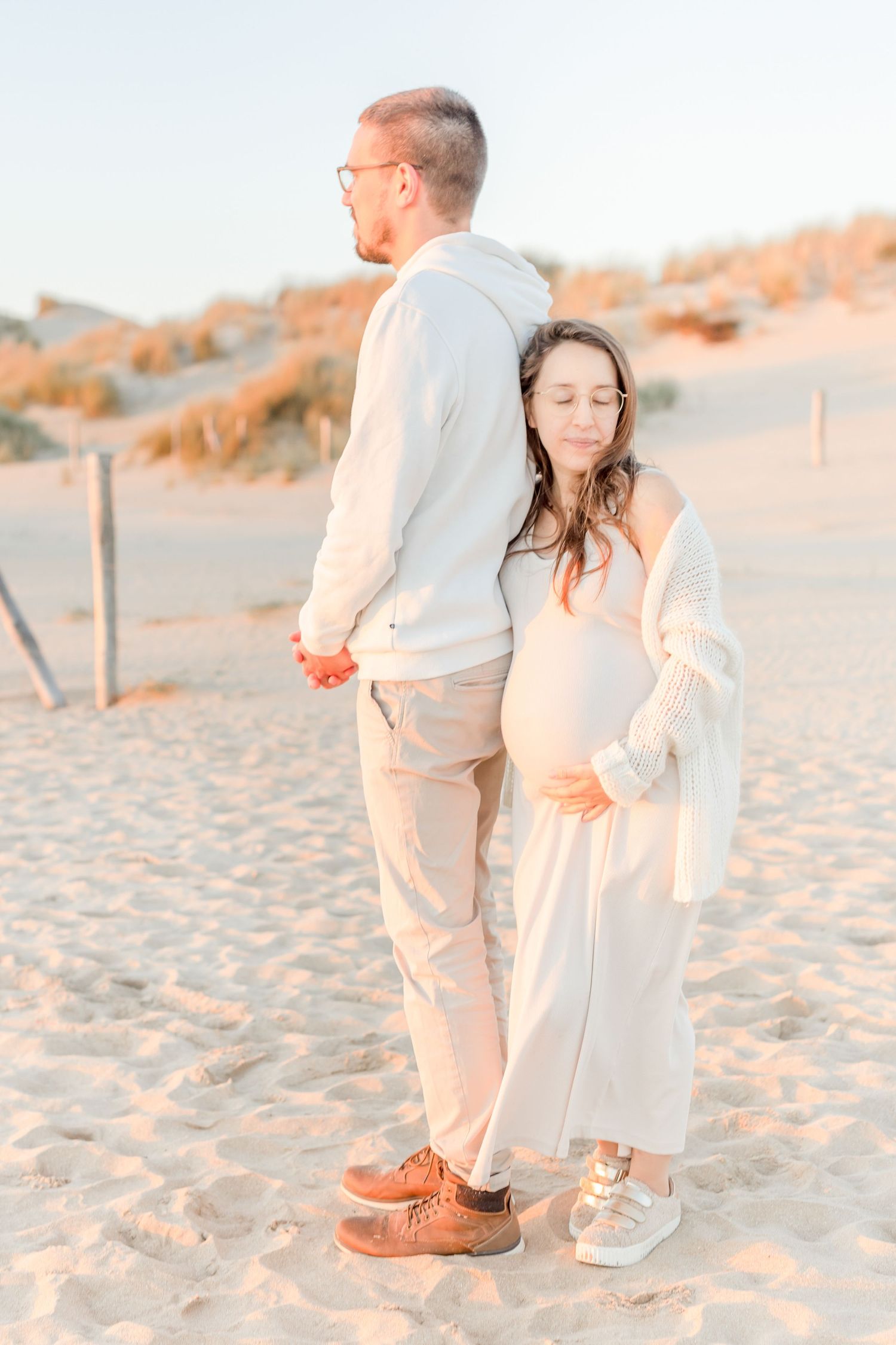 A couple stands together on sandy beach during golden hour.
