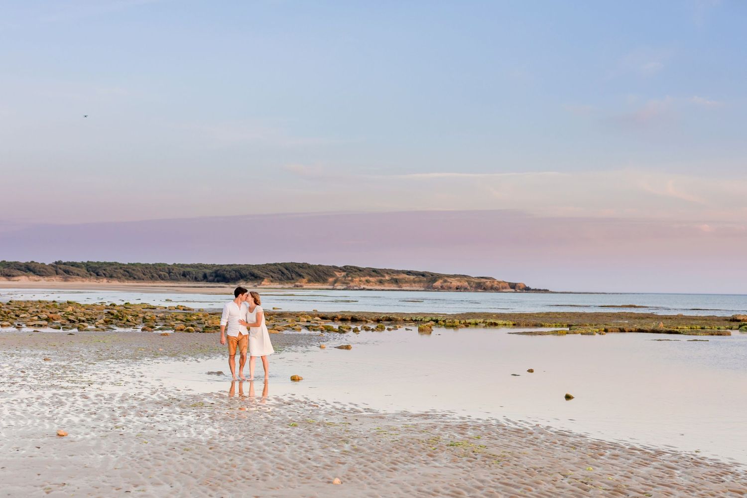 A distant couple walks along a pristine white sand beach with gentle waves in the background.