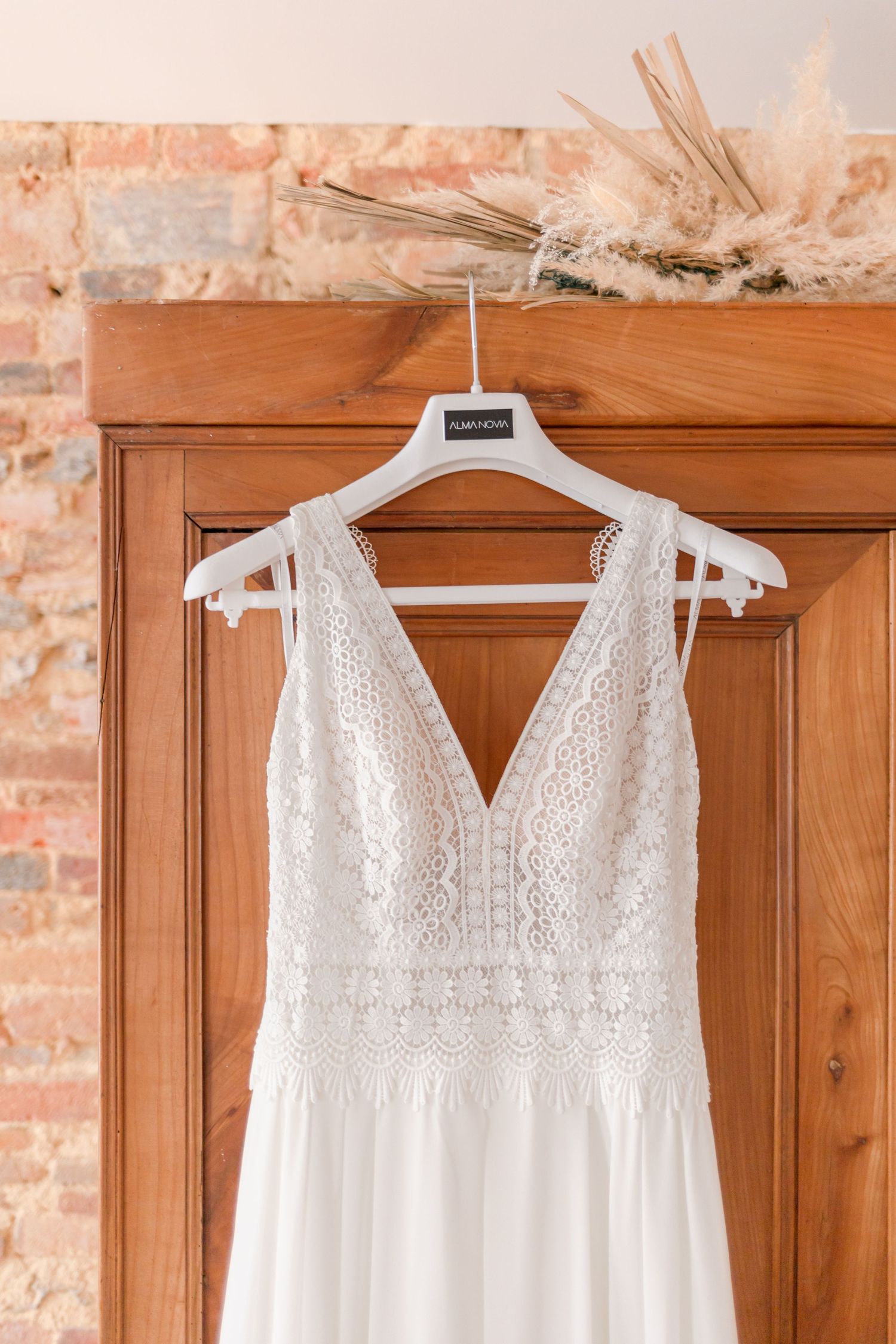 Elegant white lace wedding dress hanging on wooden door with intricate bodice detail.