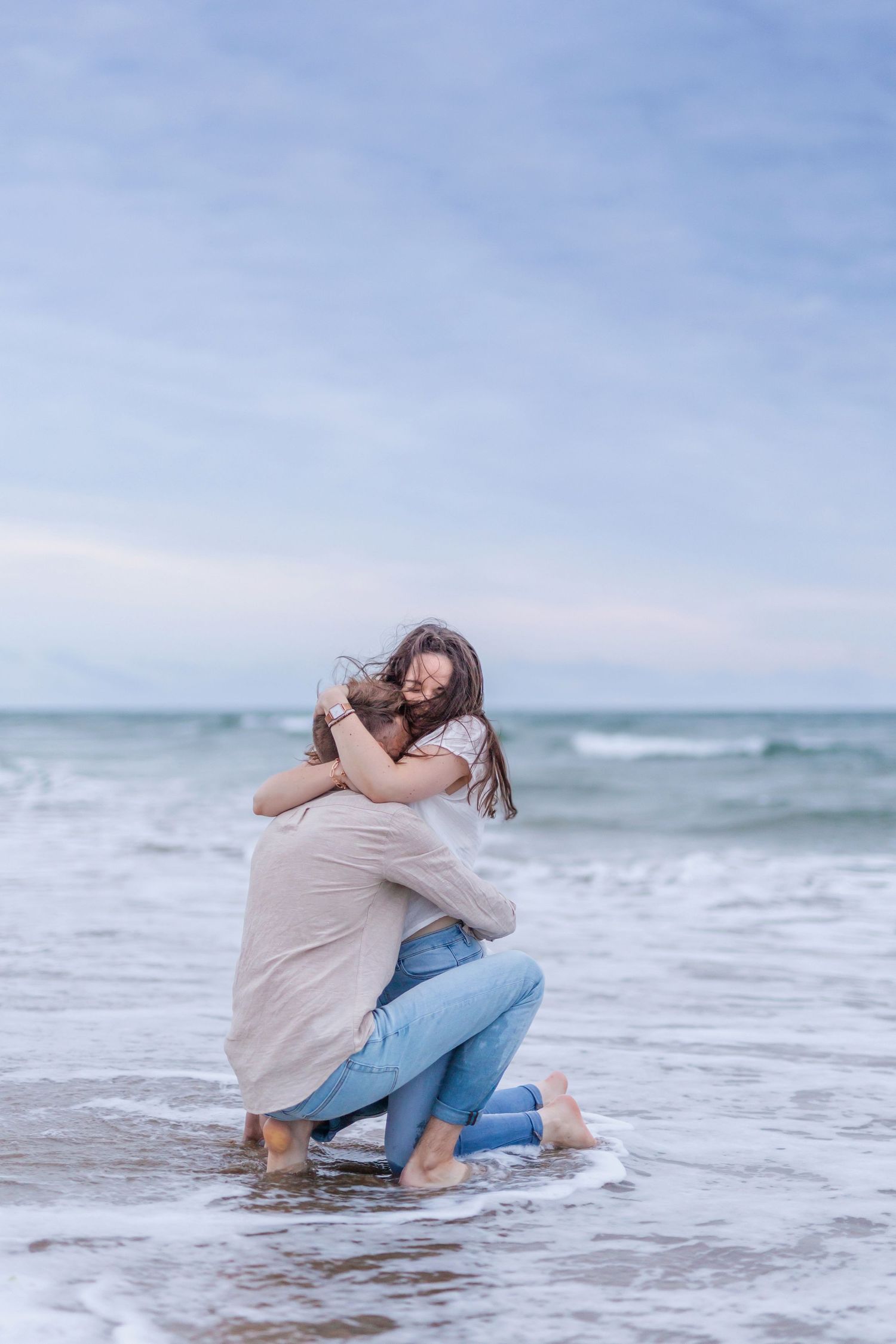 Two people share an intimate moment while kneeling in shallow ocean waves.