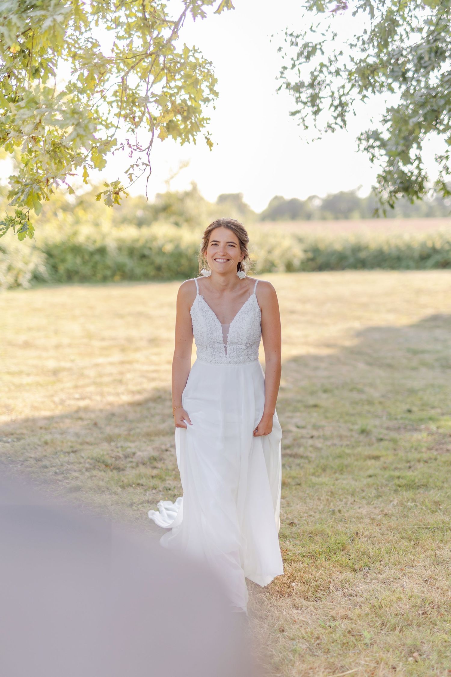 Bride in elegant v-neck wedding gown stands in golden sunlit field.