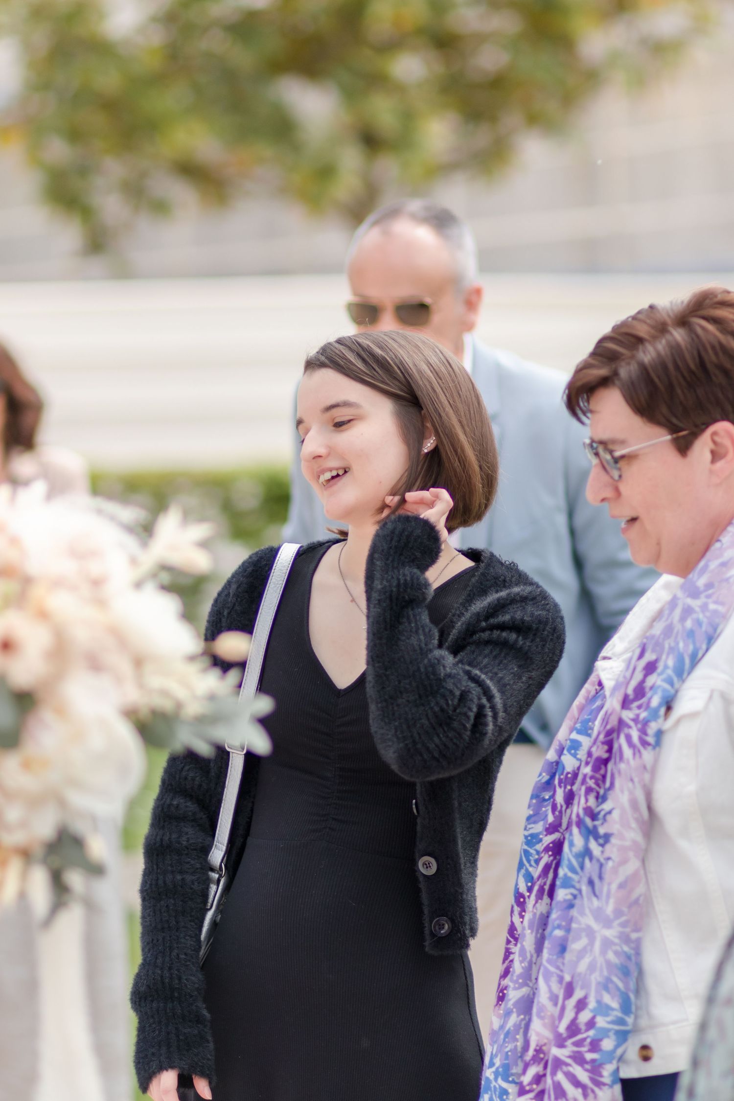 Group of wedding attendees in dark and floral attire stand together during an outdoor ceremony.