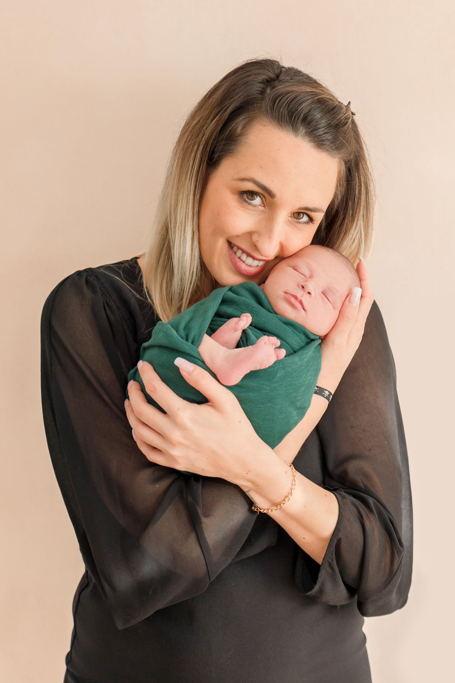 Tender moment with baby wrapped in emerald green swaddle against neutral background.