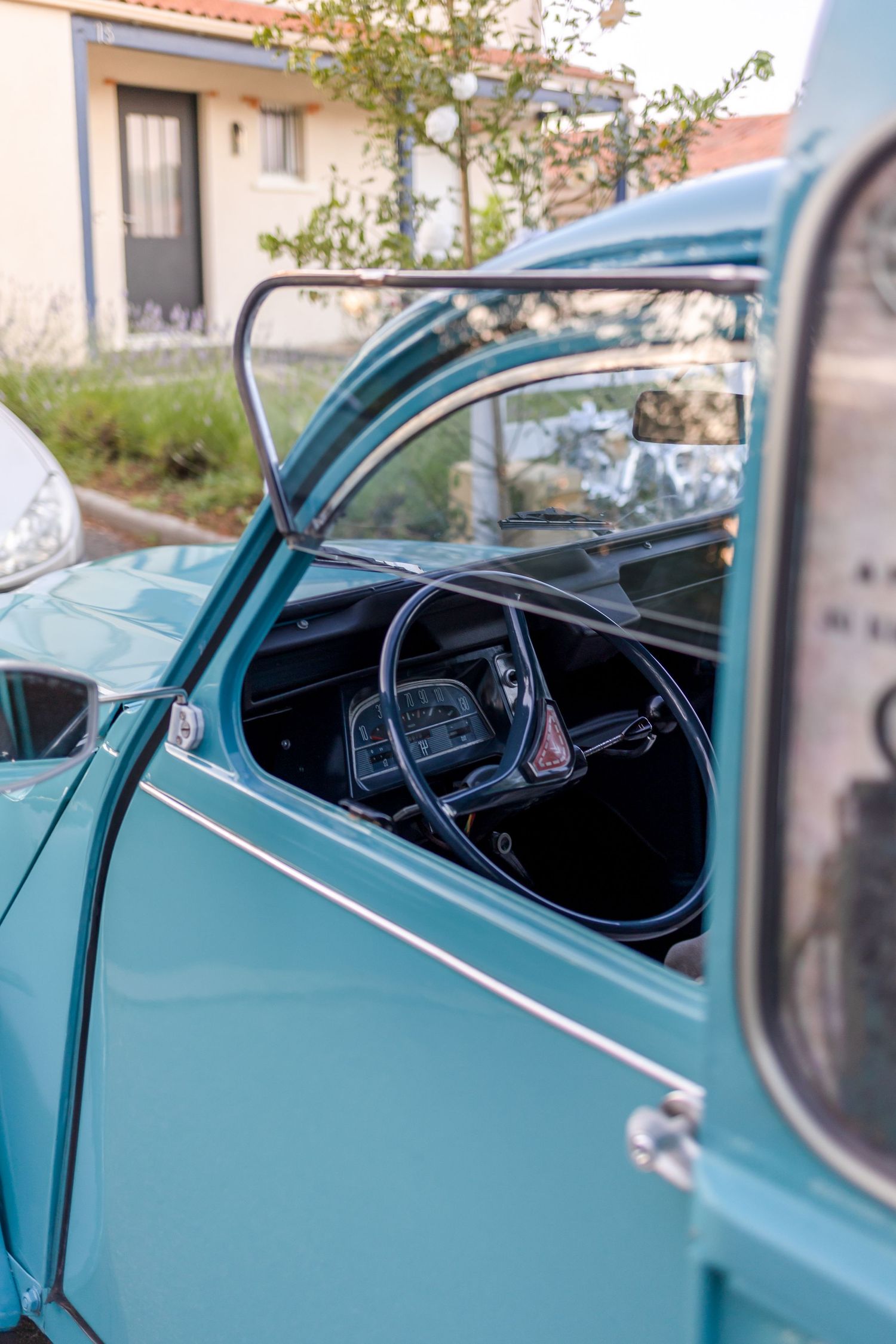 Vintage turquoise car interior showing classic steering wheel through open window.