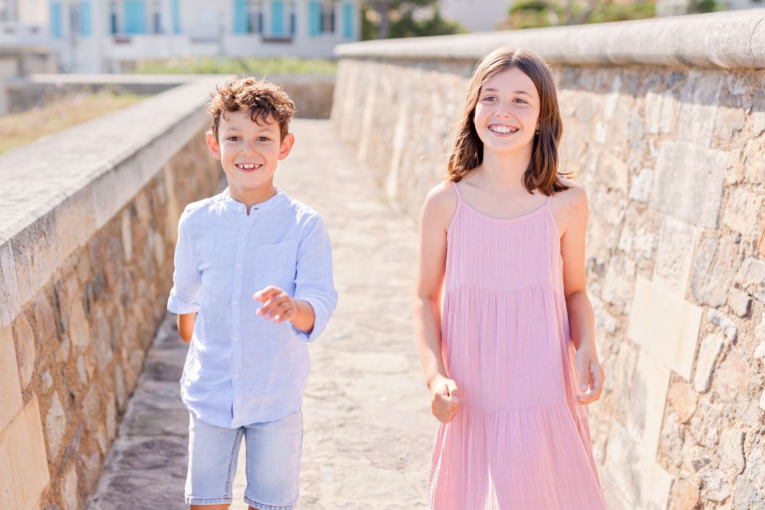 Children in light summer clothing walking along stone wall pathway.