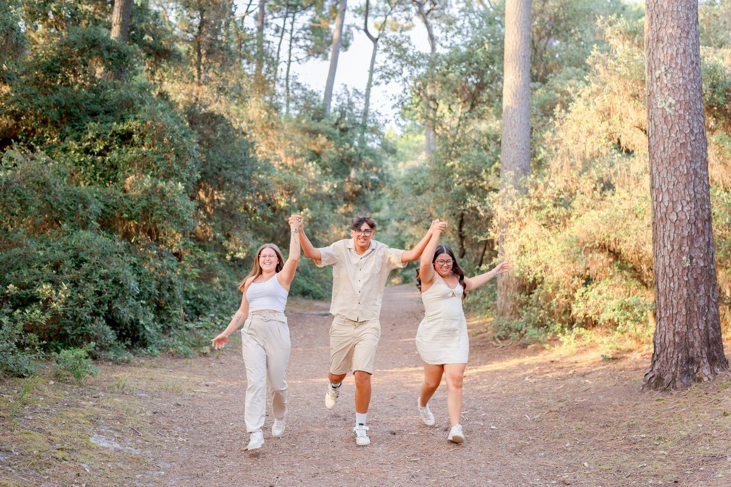 Three friends joyfully jumping and celebrating together on a sunlit forest path.