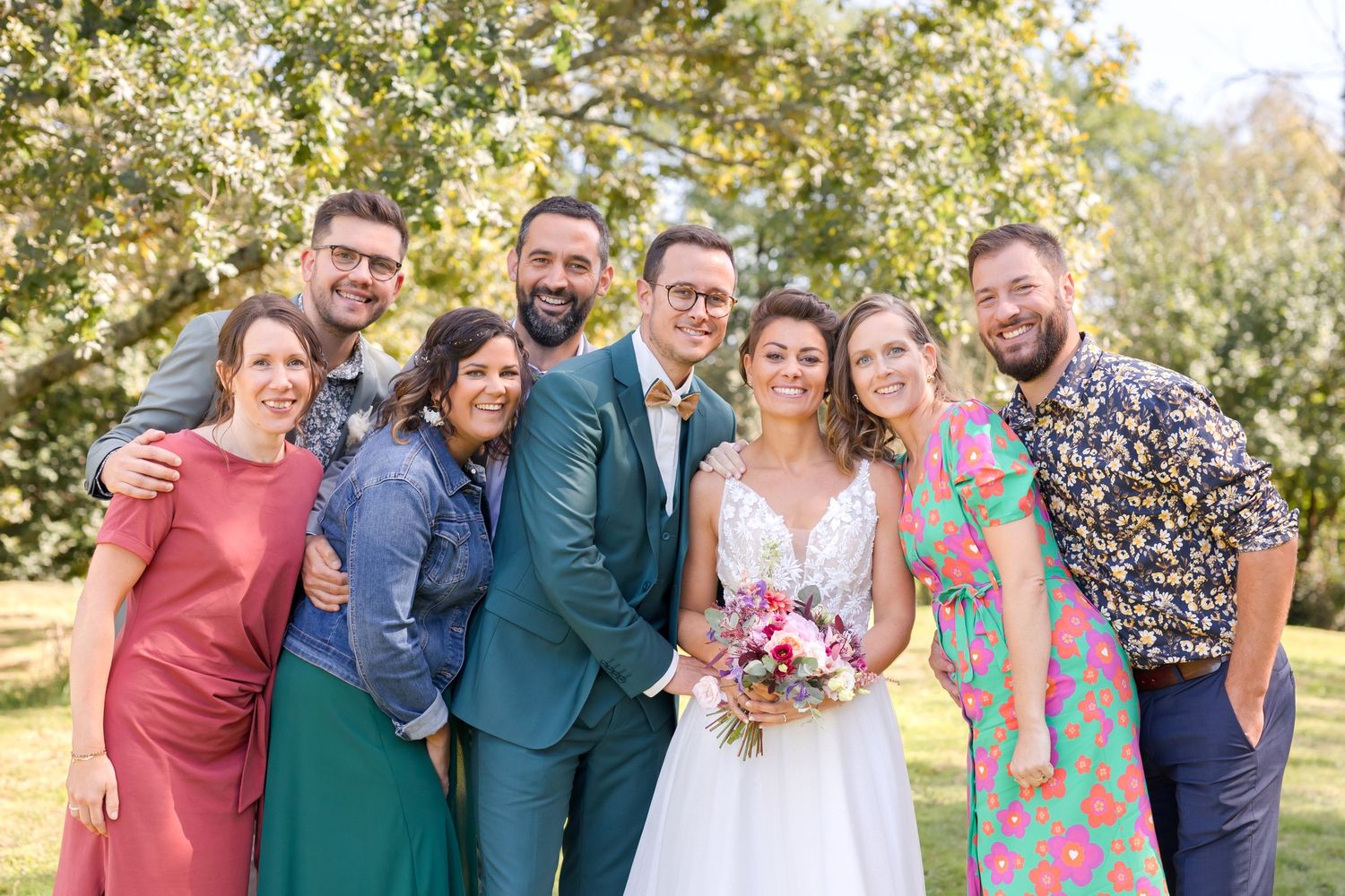 Wedding party gathered outdoors wearing teal and floral outfits for group photos.