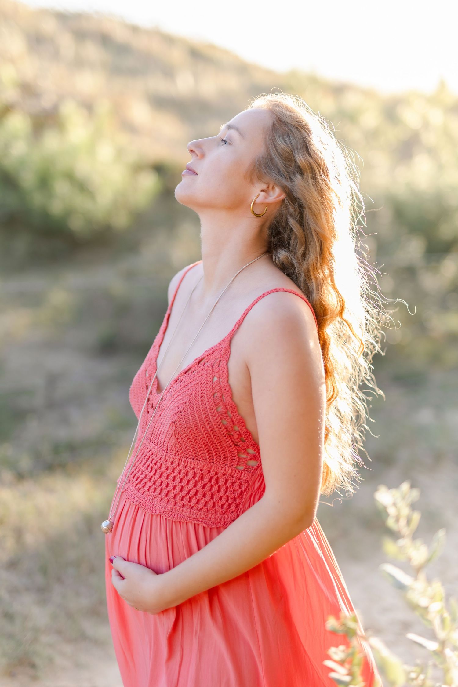 Side profile of woman in coral dress during sunset maternity photoshoot.