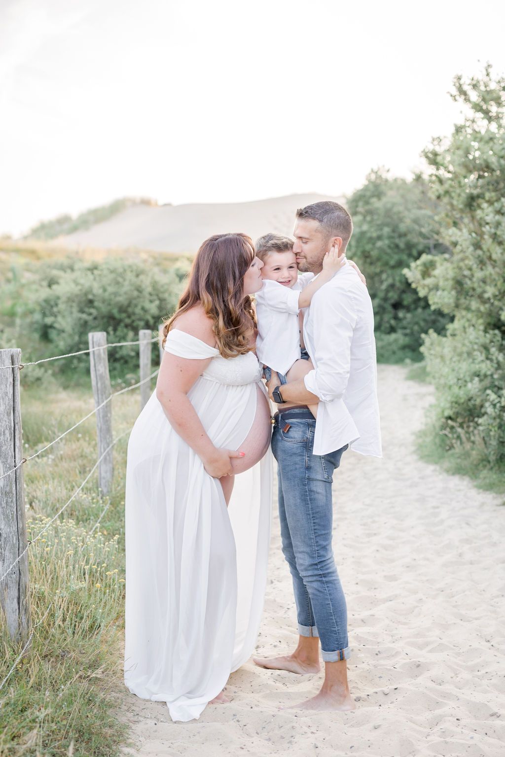 Candid family portraits along a beach walkway with wooden fence posts and coastal vegetation.