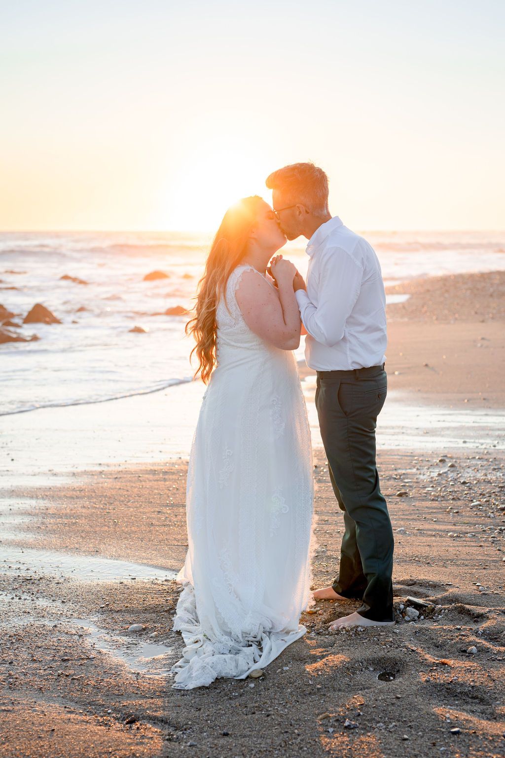 A couple shares an intimate moment on a sandy beach during golden hour.