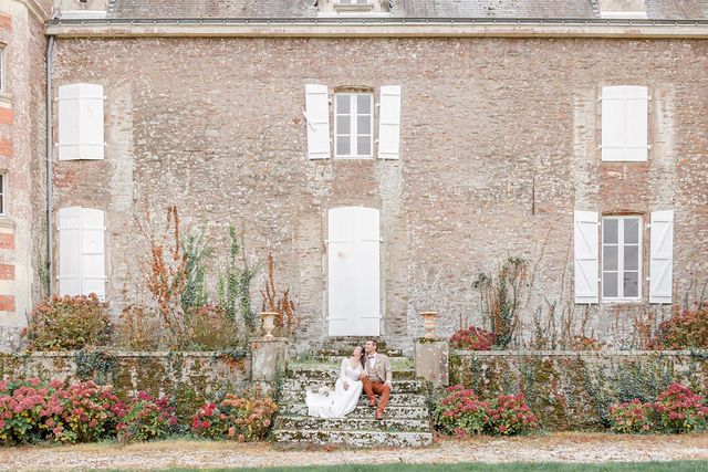 Elegant stone staircase with red blooms and climbing vines against a vintage French manor house facade.