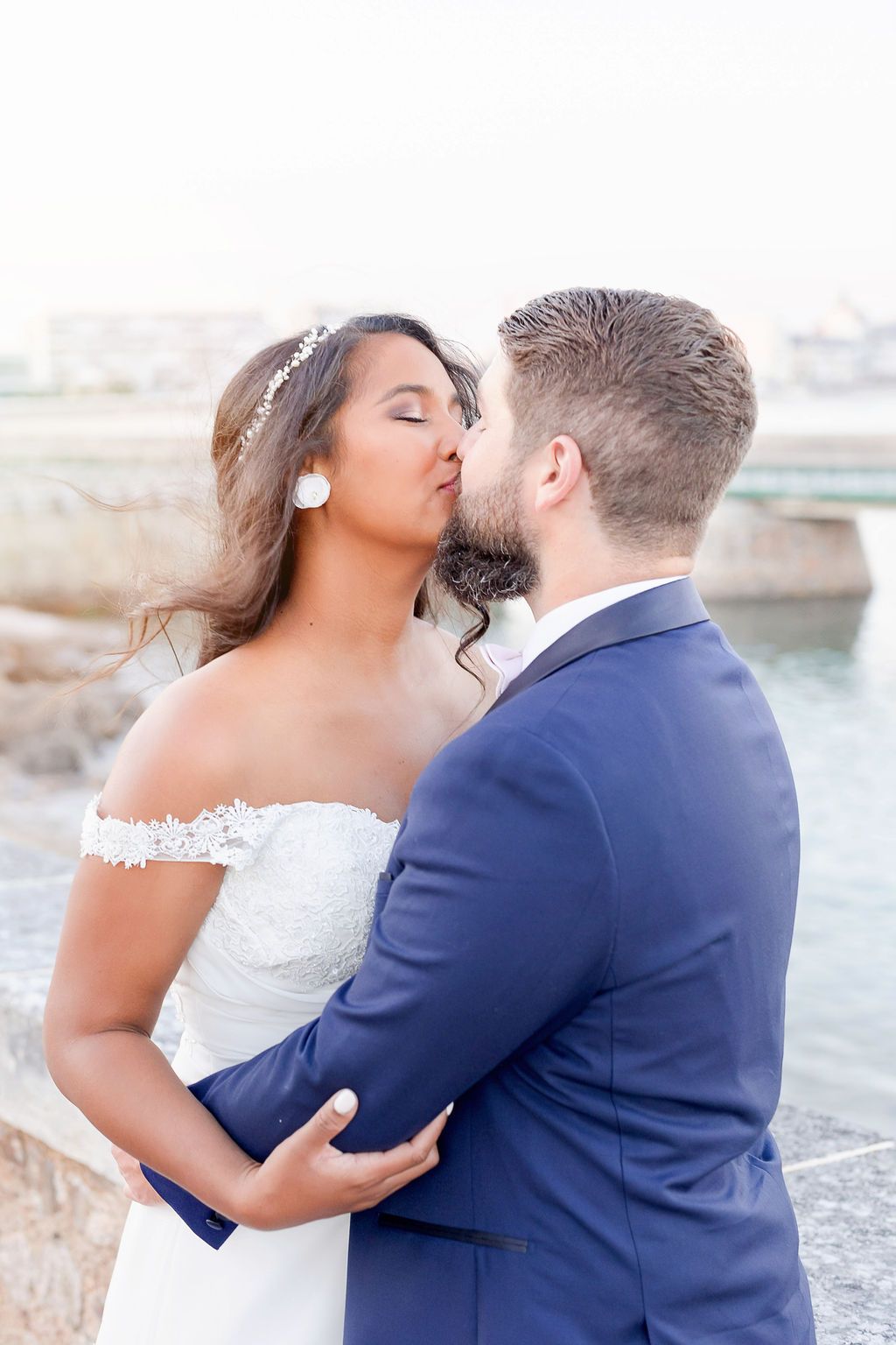 Romantic wedding couple embraces on a stone bridge with water views during golden hour.