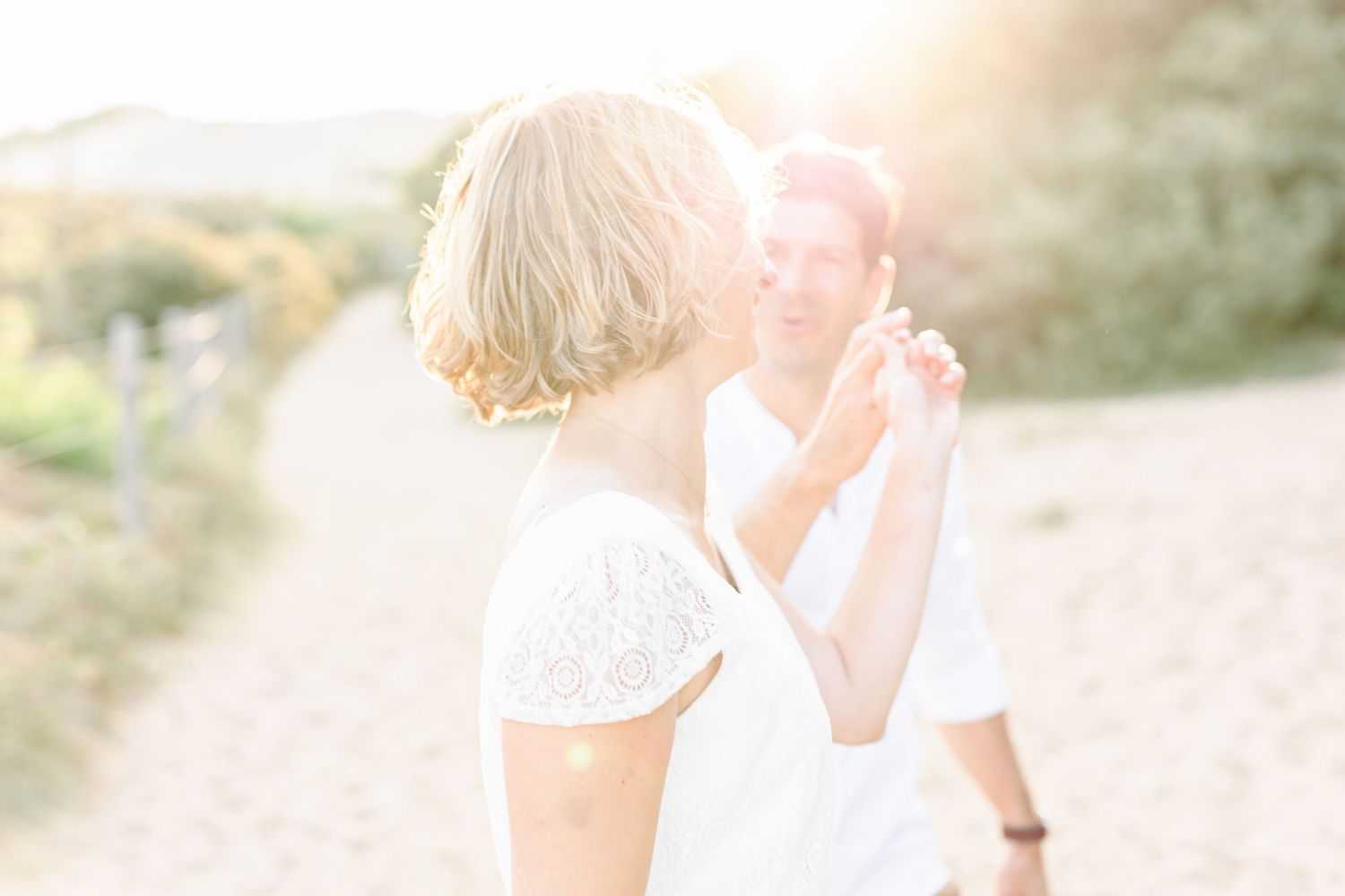 Intimate moment captured between couple in white against soft beach lighting.
