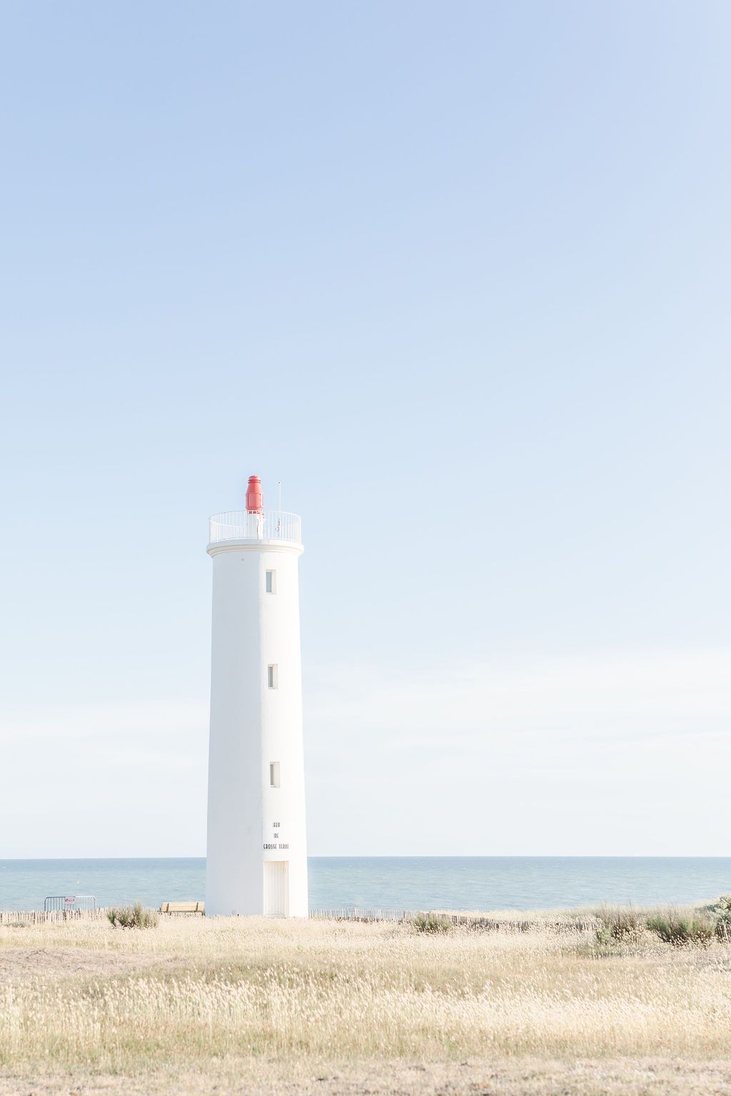 White lighthouse stands tall against clear blue sky on grassy coastal dunes.