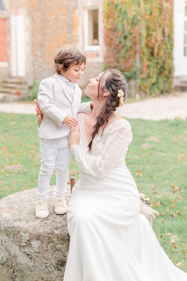 A tender wedding moment captured outdoors with elegant white attire against an ivy-covered wall.