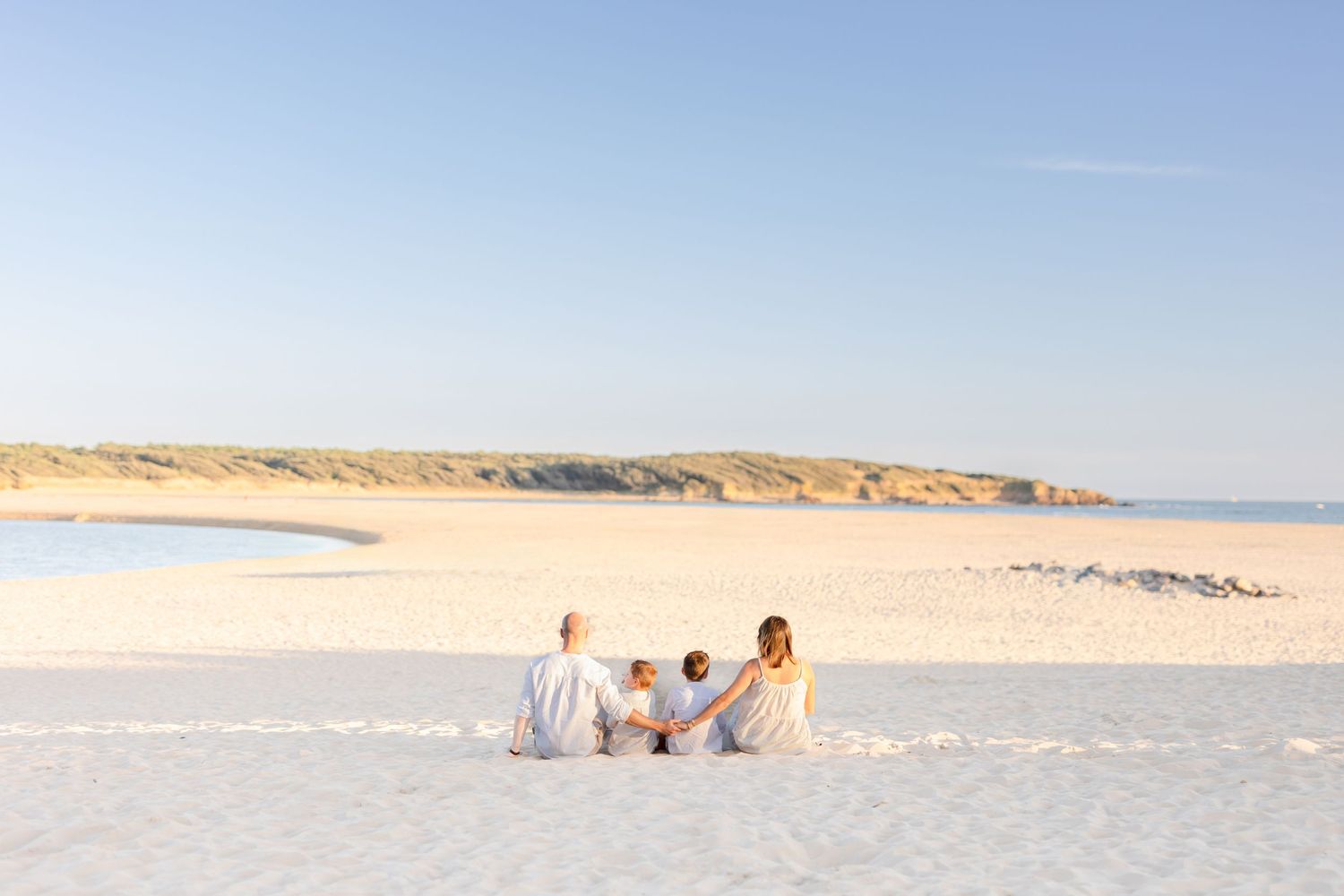 Family sitting together on white sand beach with dunes in background.
