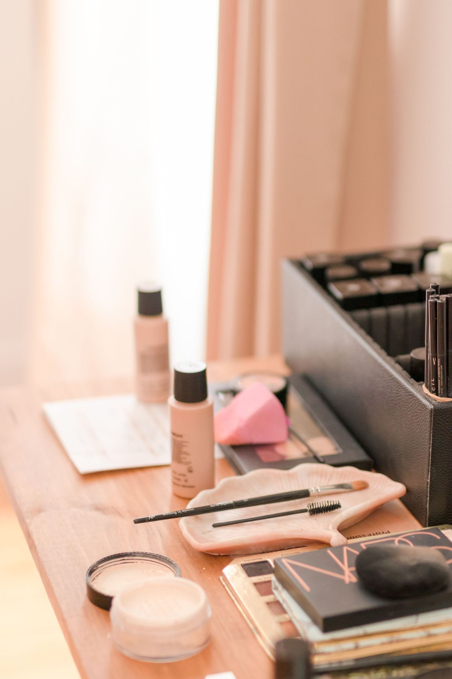 Makeup products and brushes arranged neatly on a vanity table with soft pink lighting.