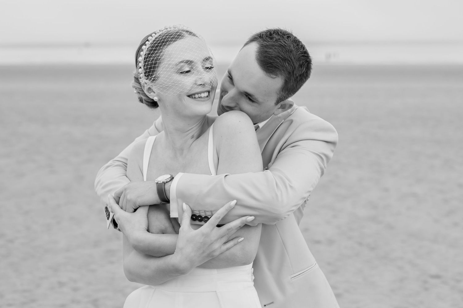 A romantic black and white portrait of a couple embracing and laughing on their wedding day.