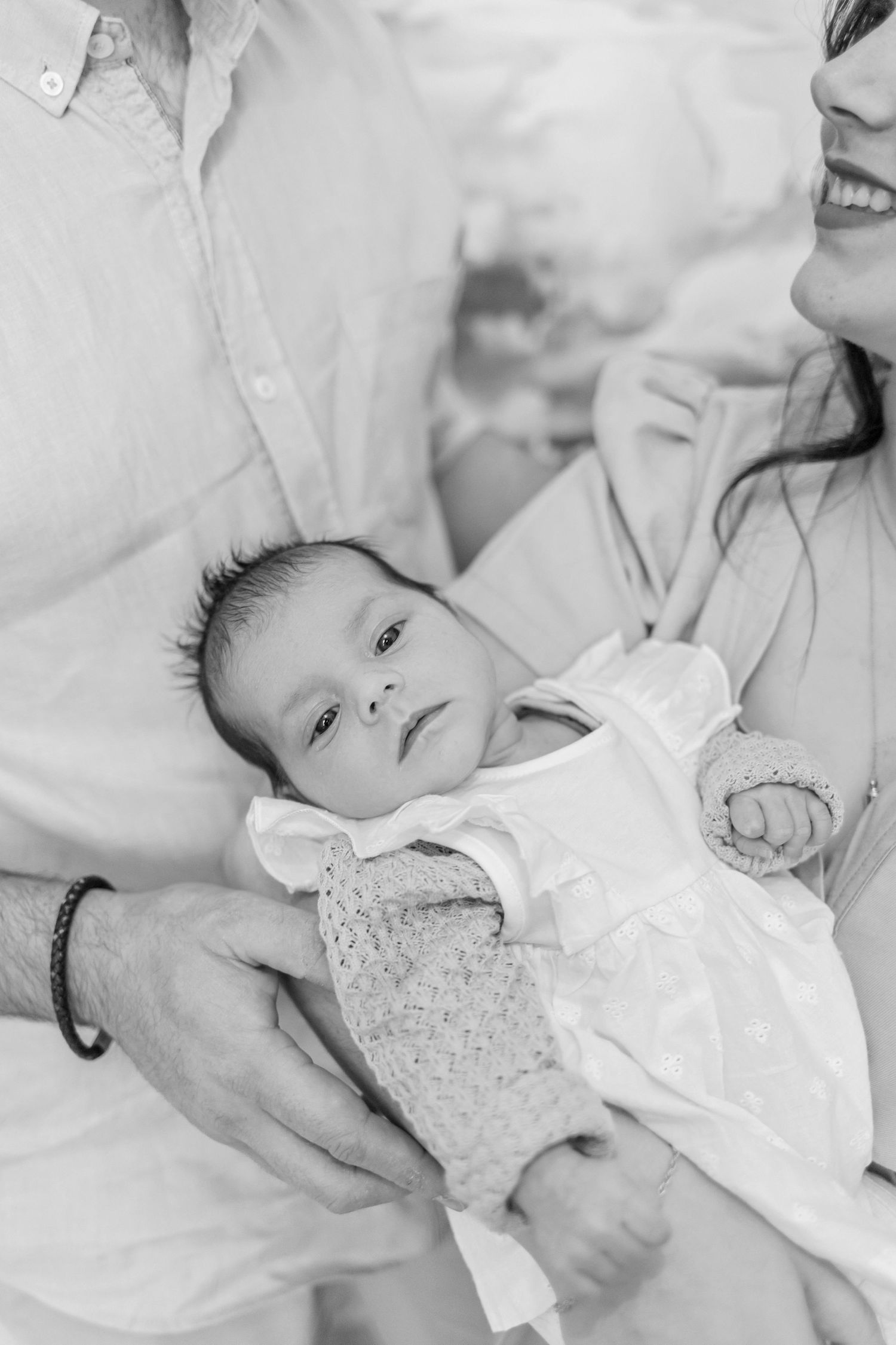 Black and white portrait of a newborn baby in white clothing being gently held.