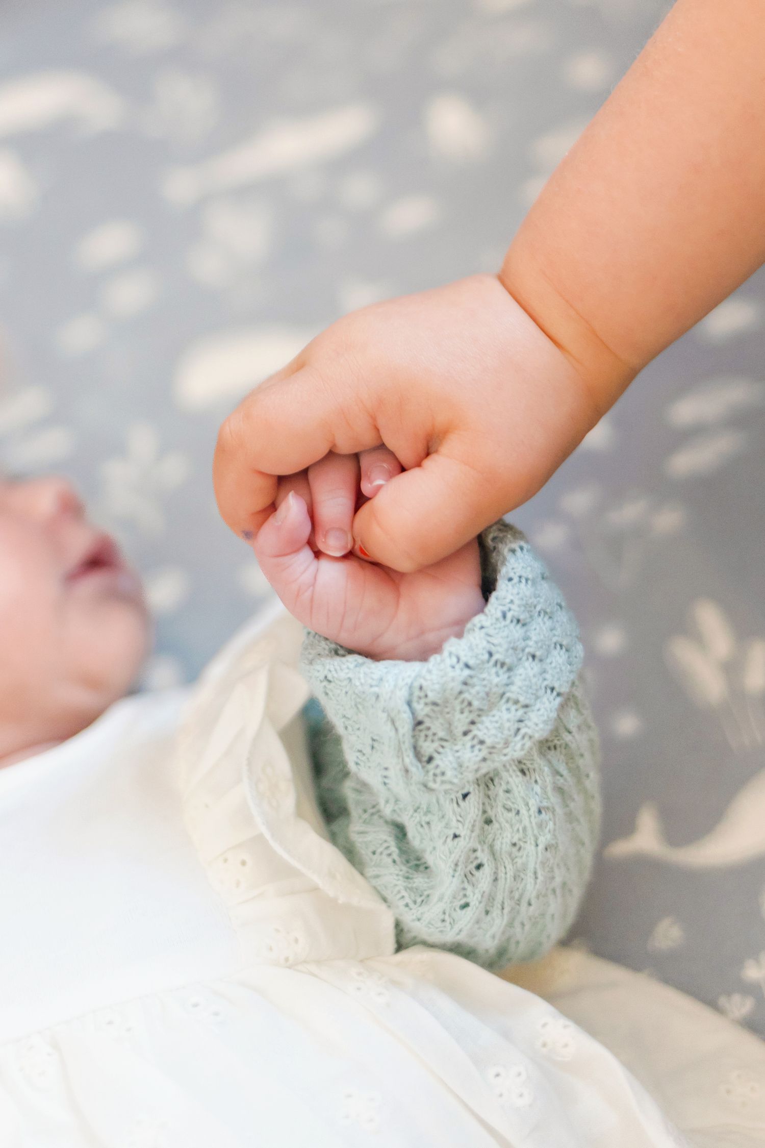 Close-up of small hand holding infant's arm wearing mint colored sweater.
