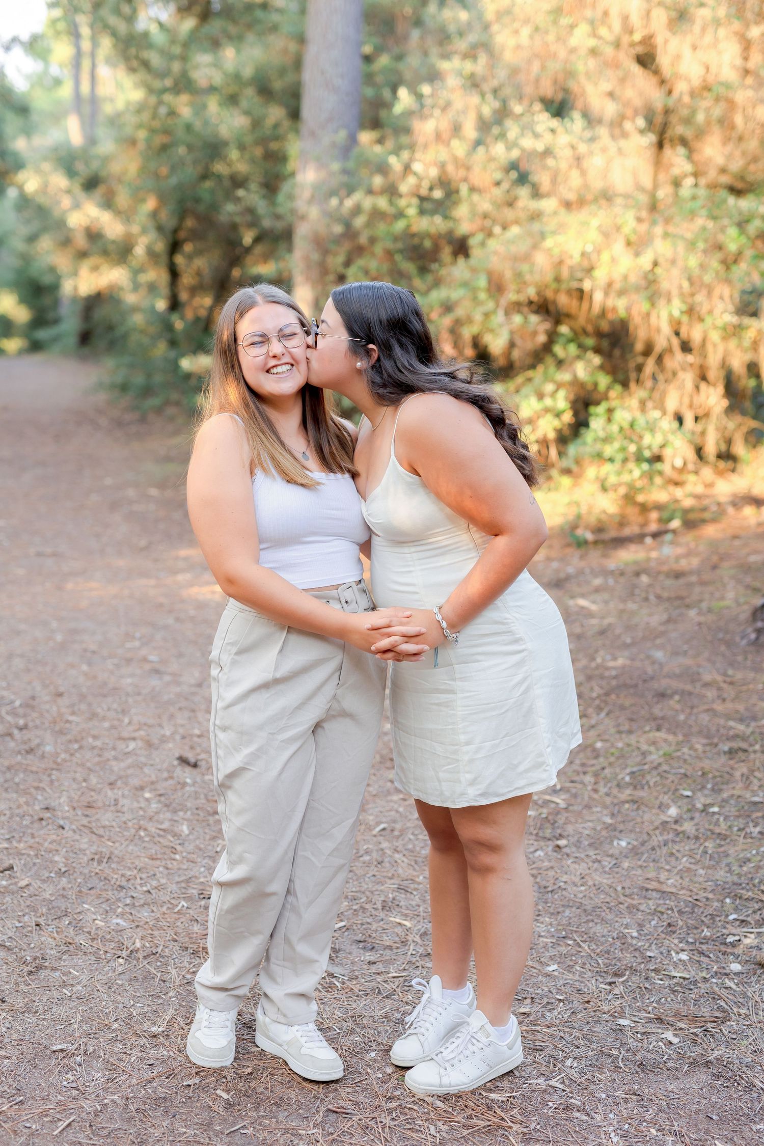 Two people in coordinated white outfits sharing an affectionate moment on a forest trail.