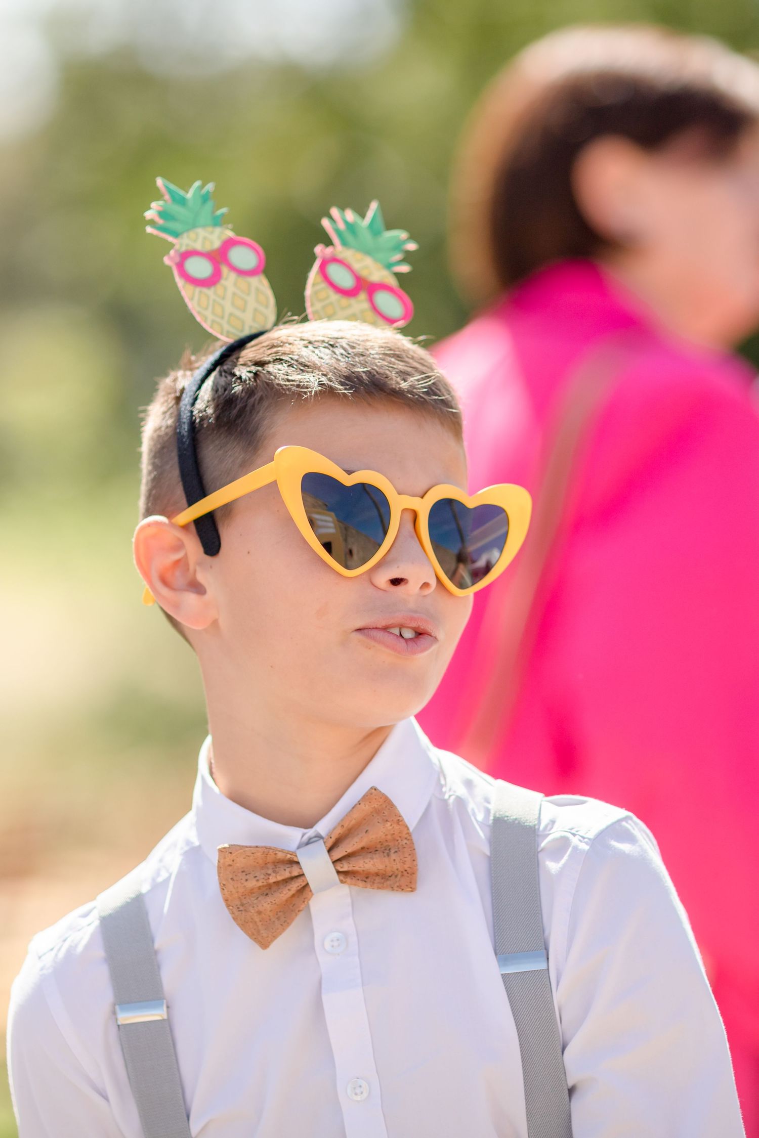 Young wedding attendant wearing heart-shaped sunglasses and pineapple headband accessories.