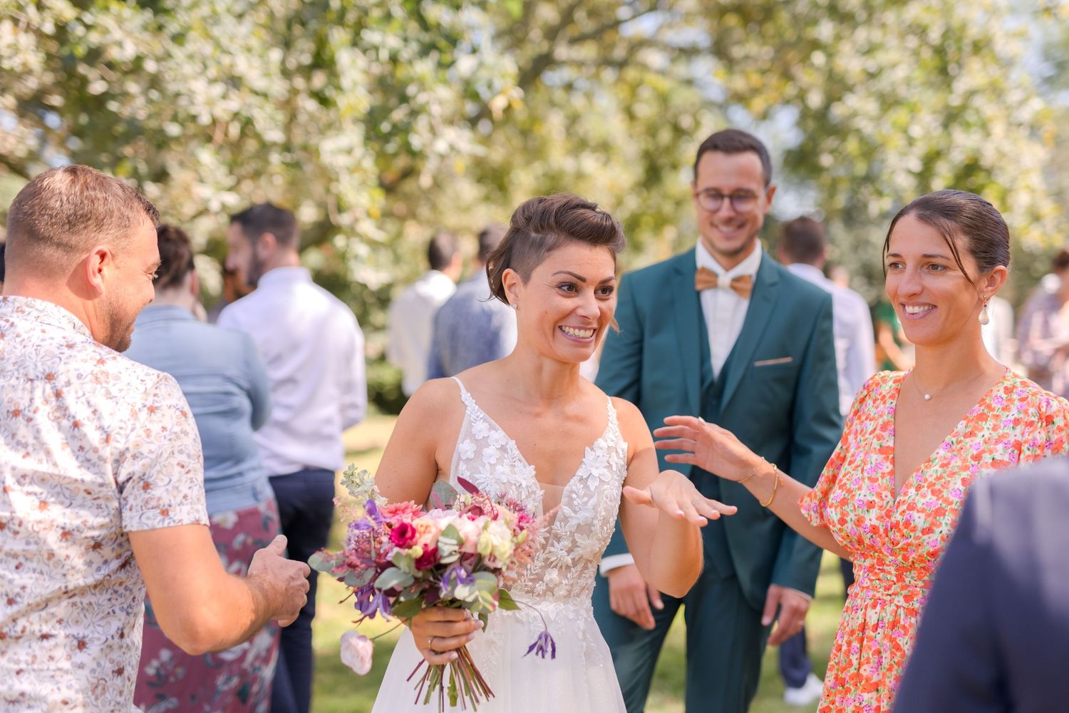 Wedding celebration in an outdoor garden setting with guests mingling and a bridal bouquet of pink flowers.