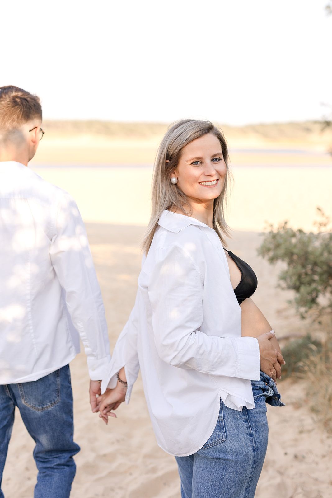 A romantic moment as a couple in white shirts and denim hold hands in a desert landscape at sunset.