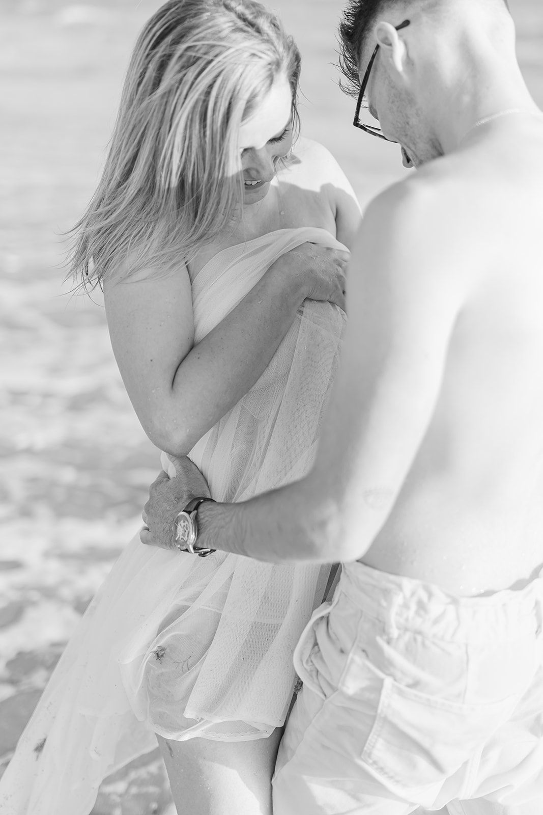A romantic black and white photograph of two people sharing an intimate embrace on a beach.