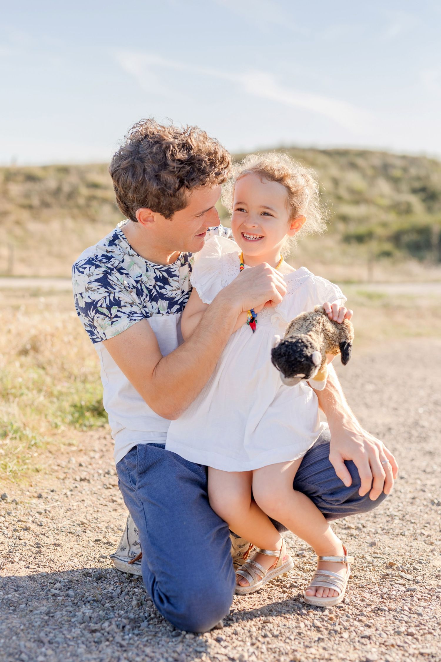 A tender family portrait on a dirt path with rolling hills in the background.