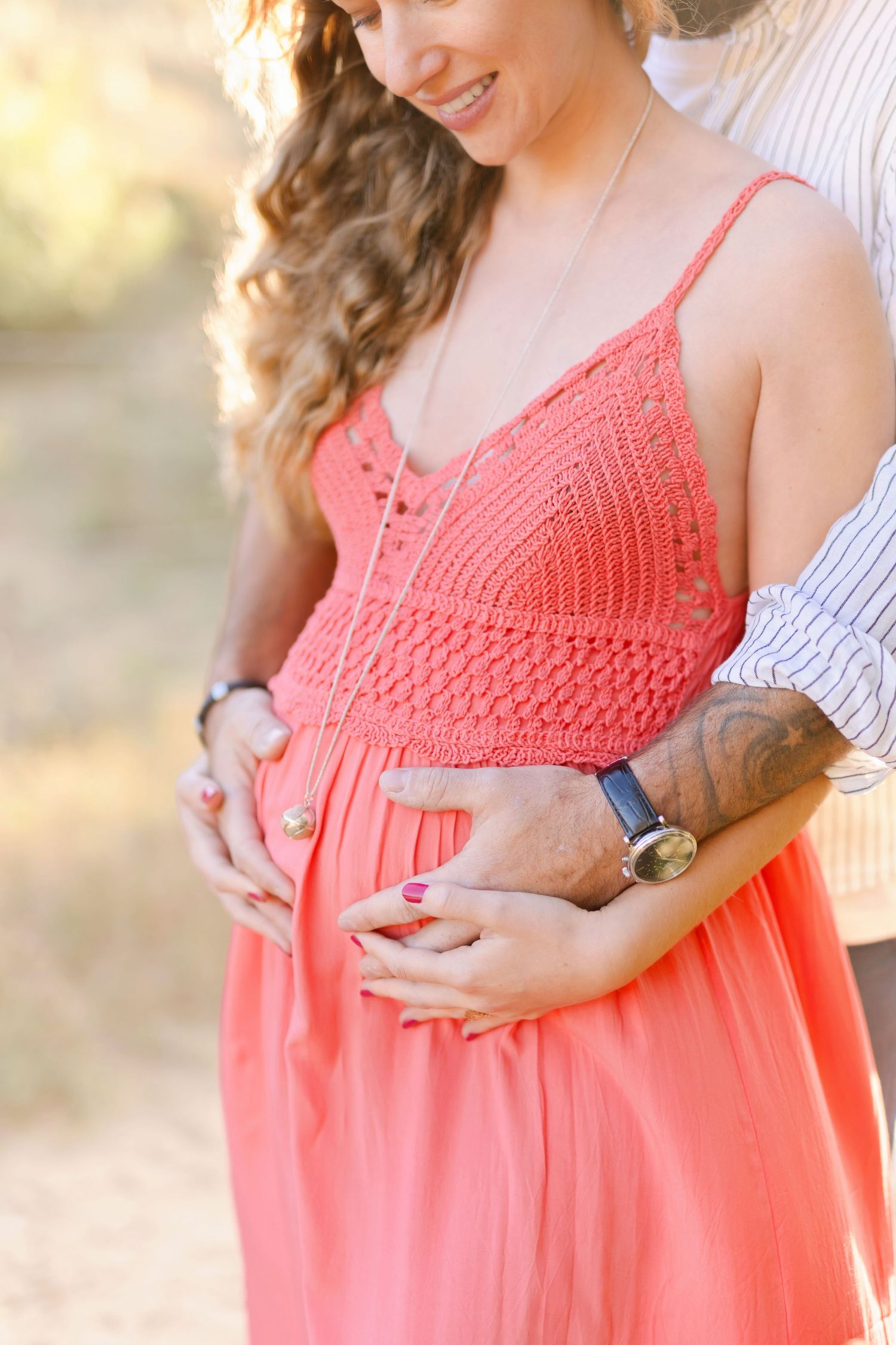 Person wearing a flowing coral sundress cradles their belly in golden sunset light.