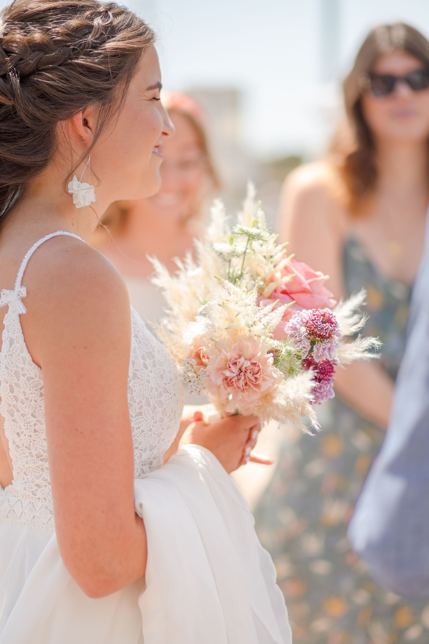 A close-up view of a bridal bouquet featuring soft peach and pink flowers in natural sunlight.