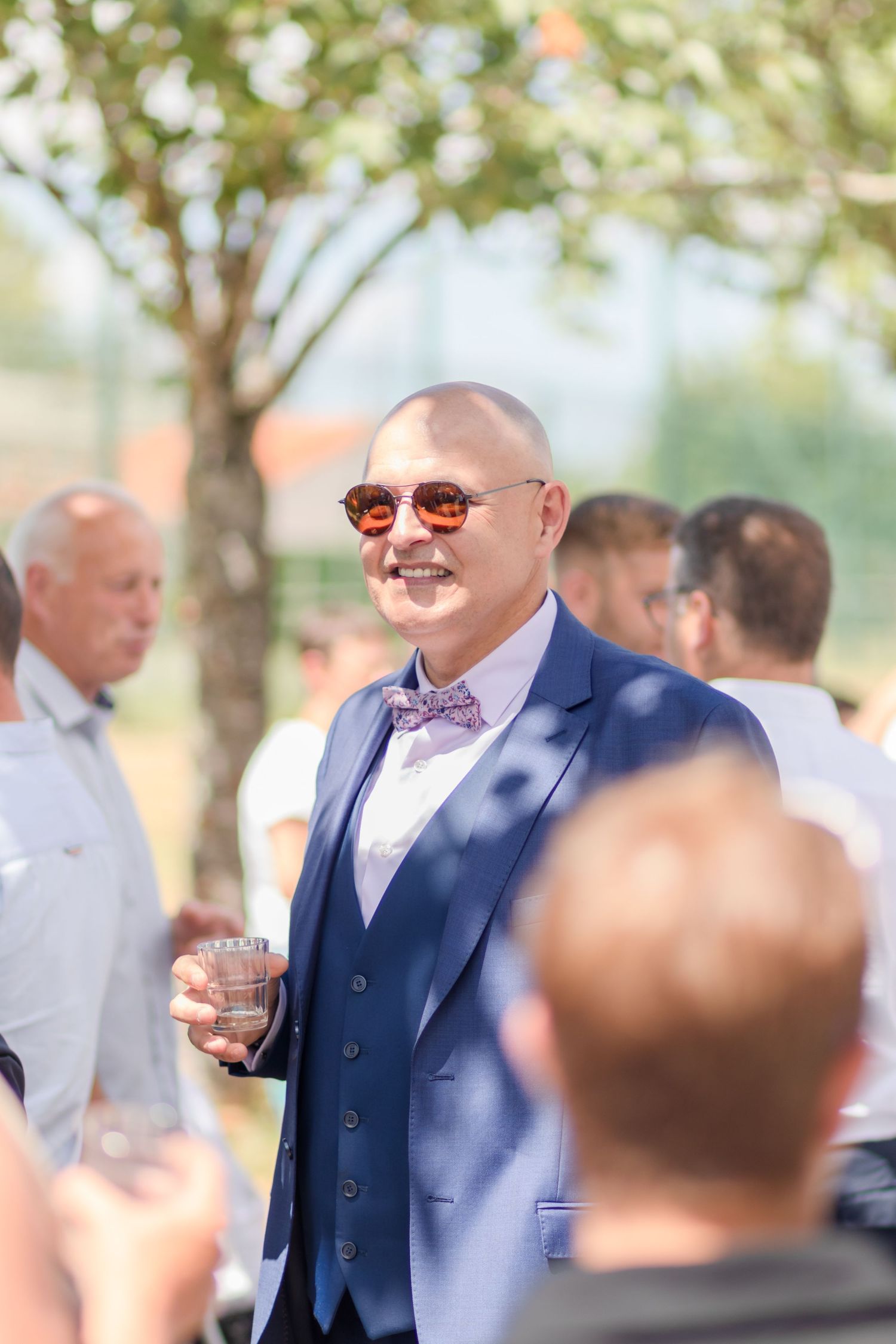 Wedding guests mingling outdoors in formal attire during sunny daytime celebration.