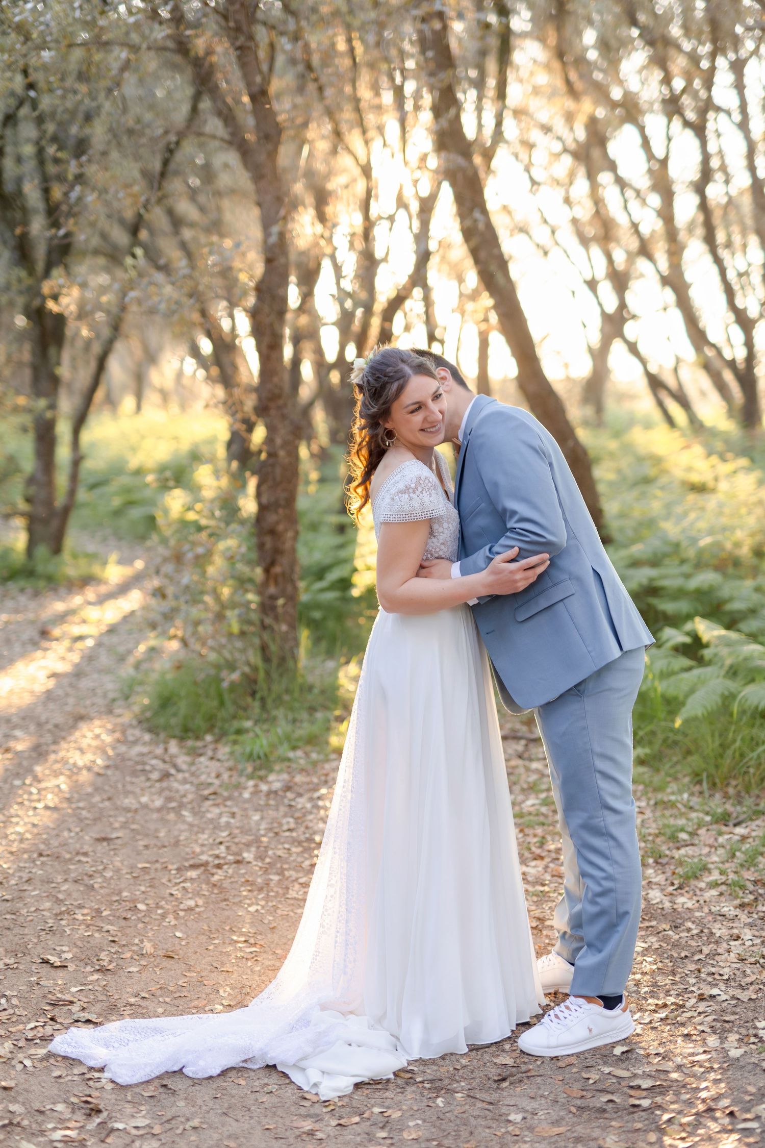 A sweet embrace between newlyweds on a forest path during golden hour.