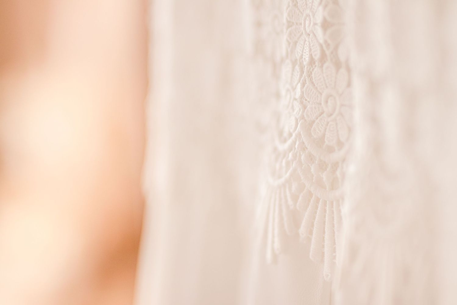 Close-up of delicate white lace pattern on wedding dress fabric.